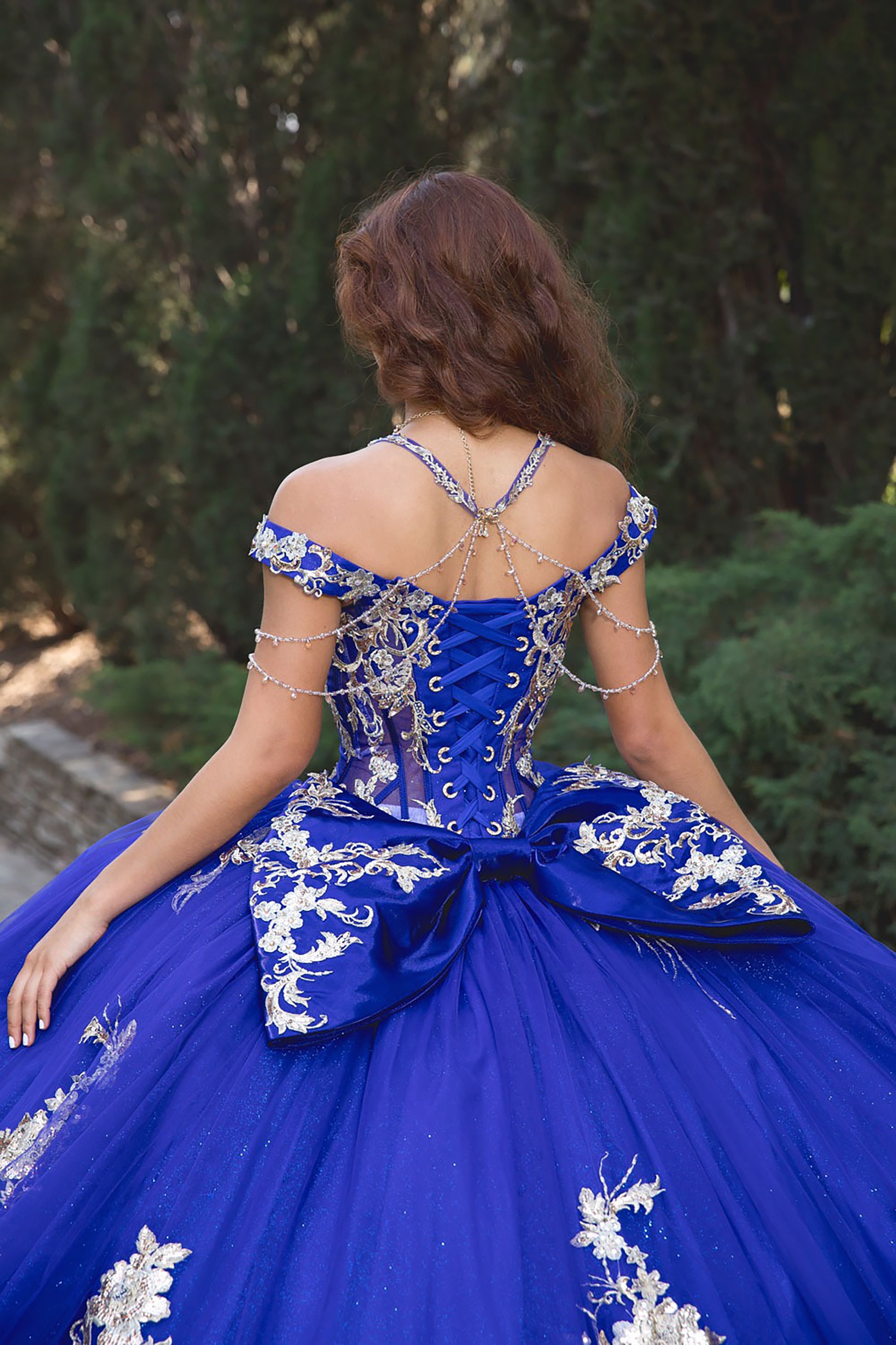 Woman wearing a blue and white formal dress with intricate detailing in an outdoor setting.