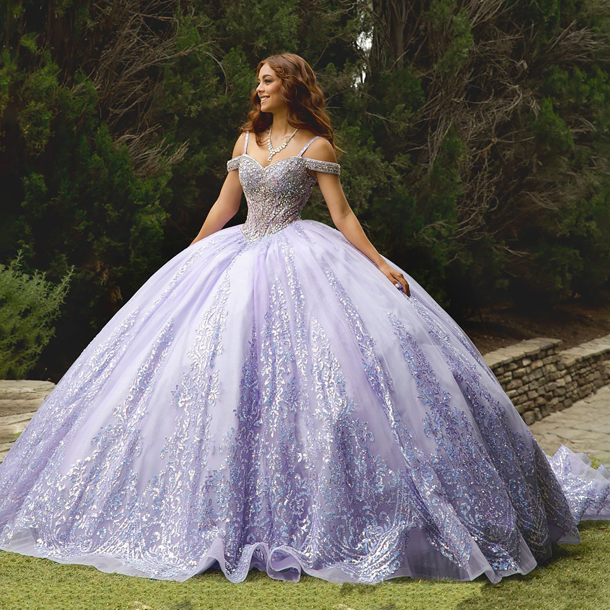 Woman in a sparkling purple gown standing outdoors with greenery in the background