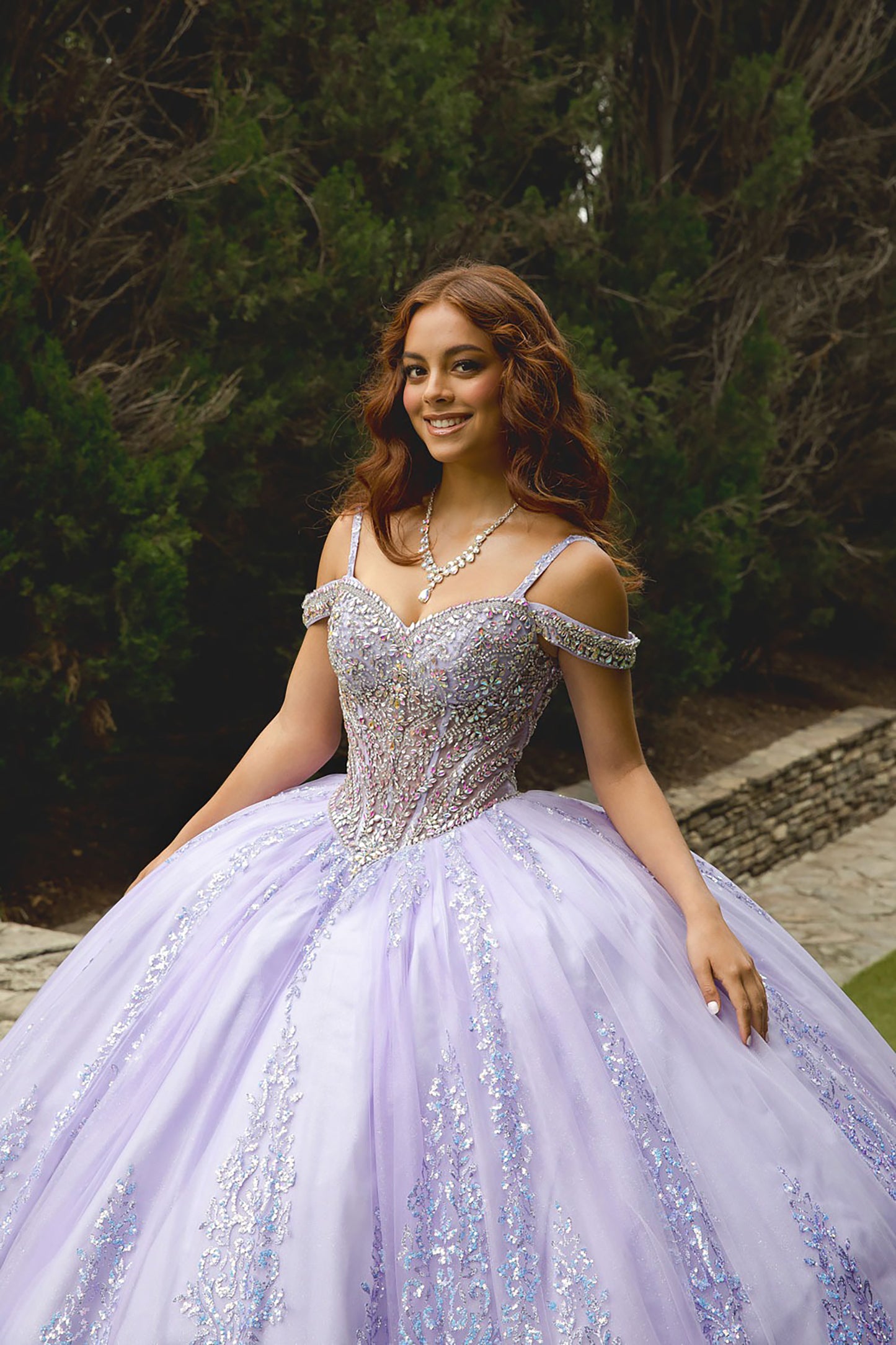 Woman in a sparkling purple gown outdoors with greenery in the background