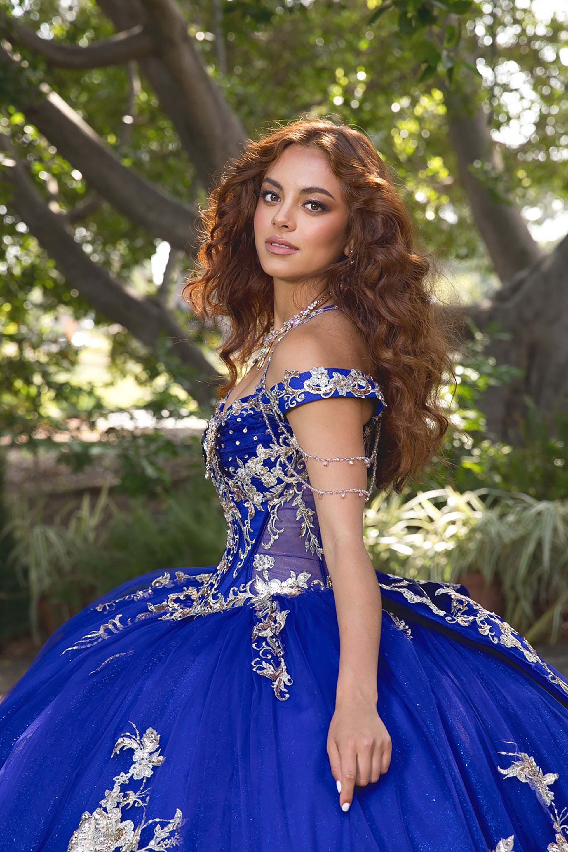 Woman in a blue and silver dress standing outdoors with greenery in the background