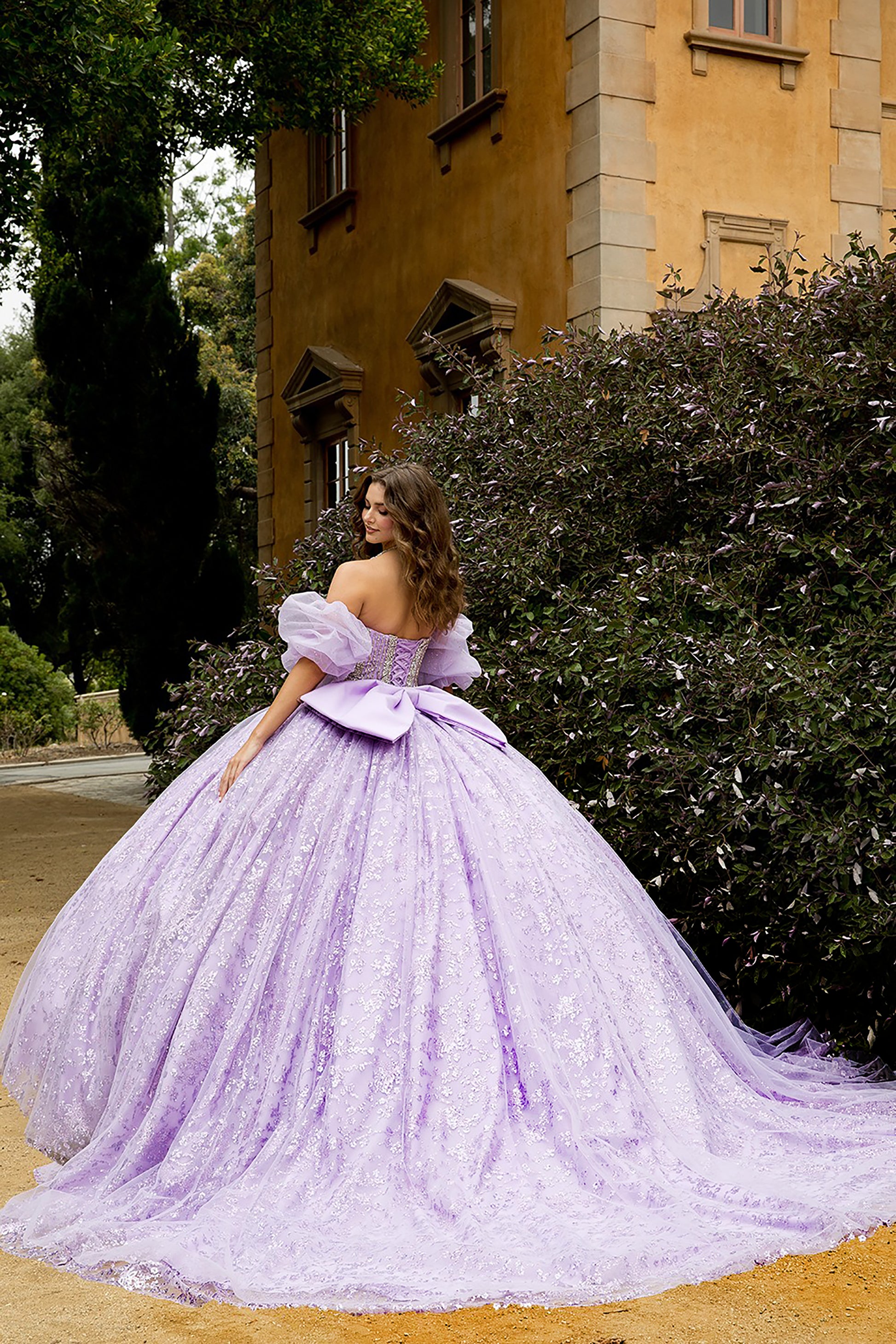 Woman in a purple gown standing in front of a building with greenery