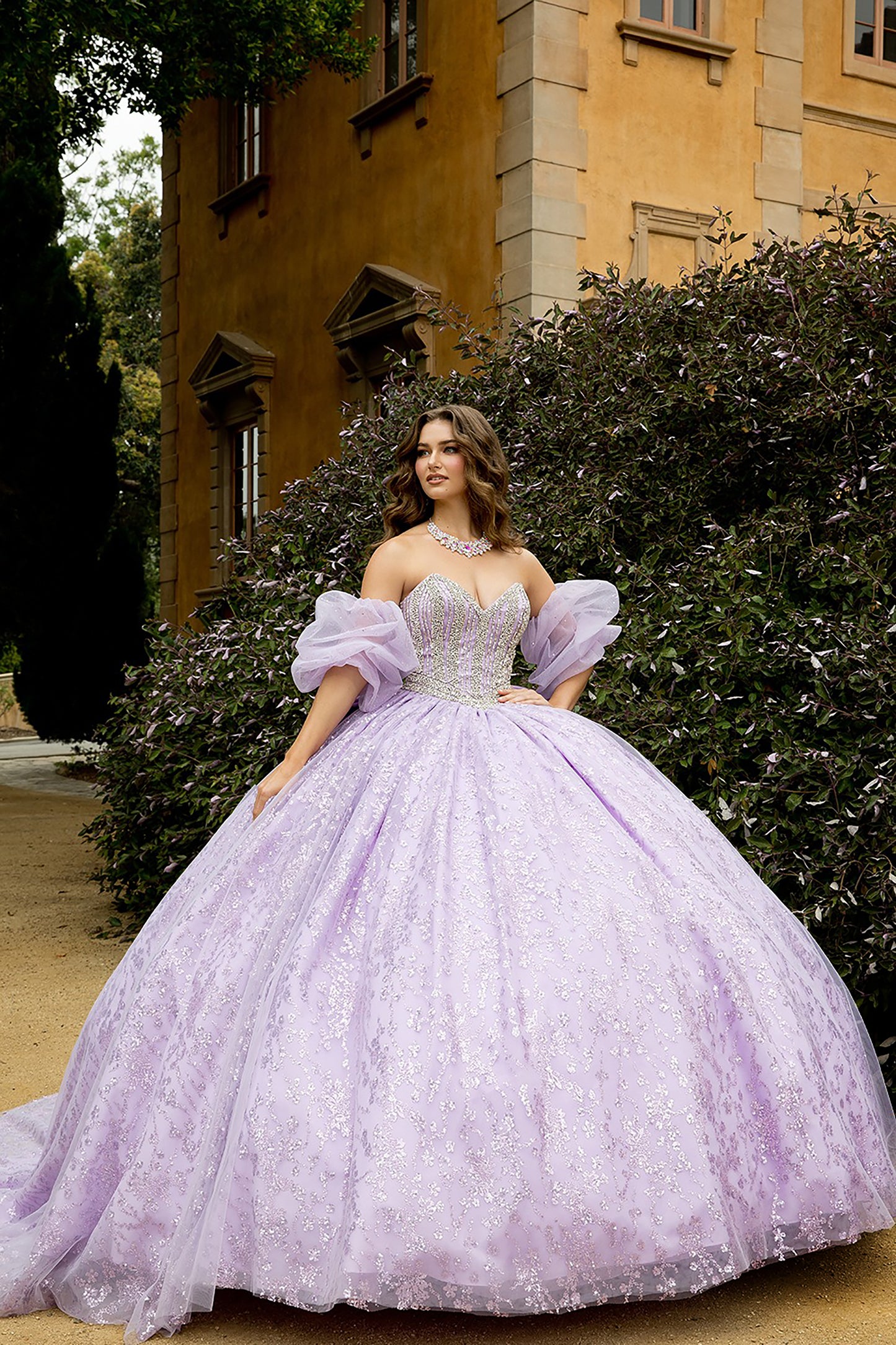Woman in a lavender gown standing in front of a building with greenery