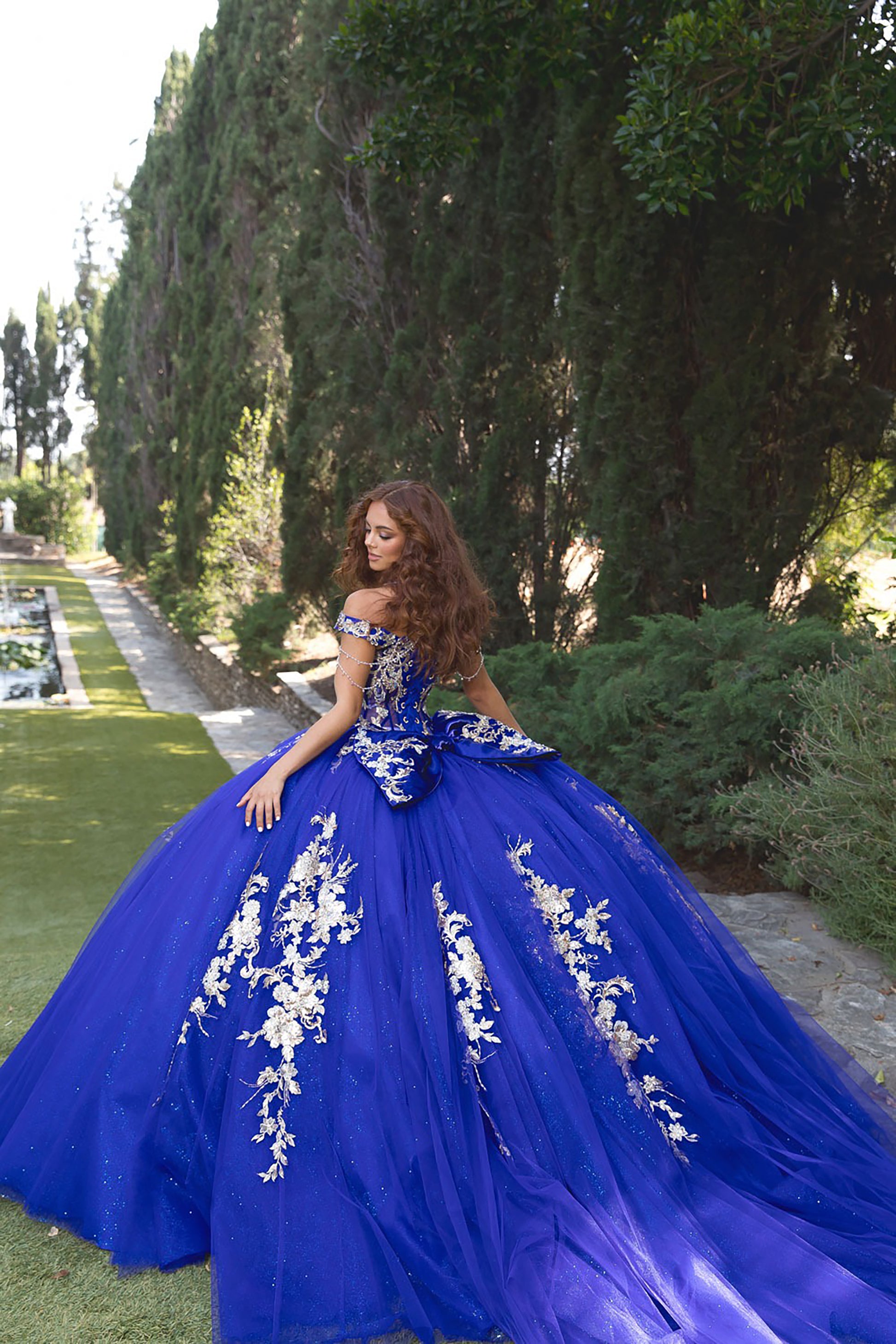Woman in a blue evening gown with floral details standing outdoors.