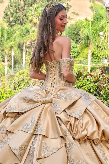 Woman in a beige ball gown with intricate details standing outdoors.