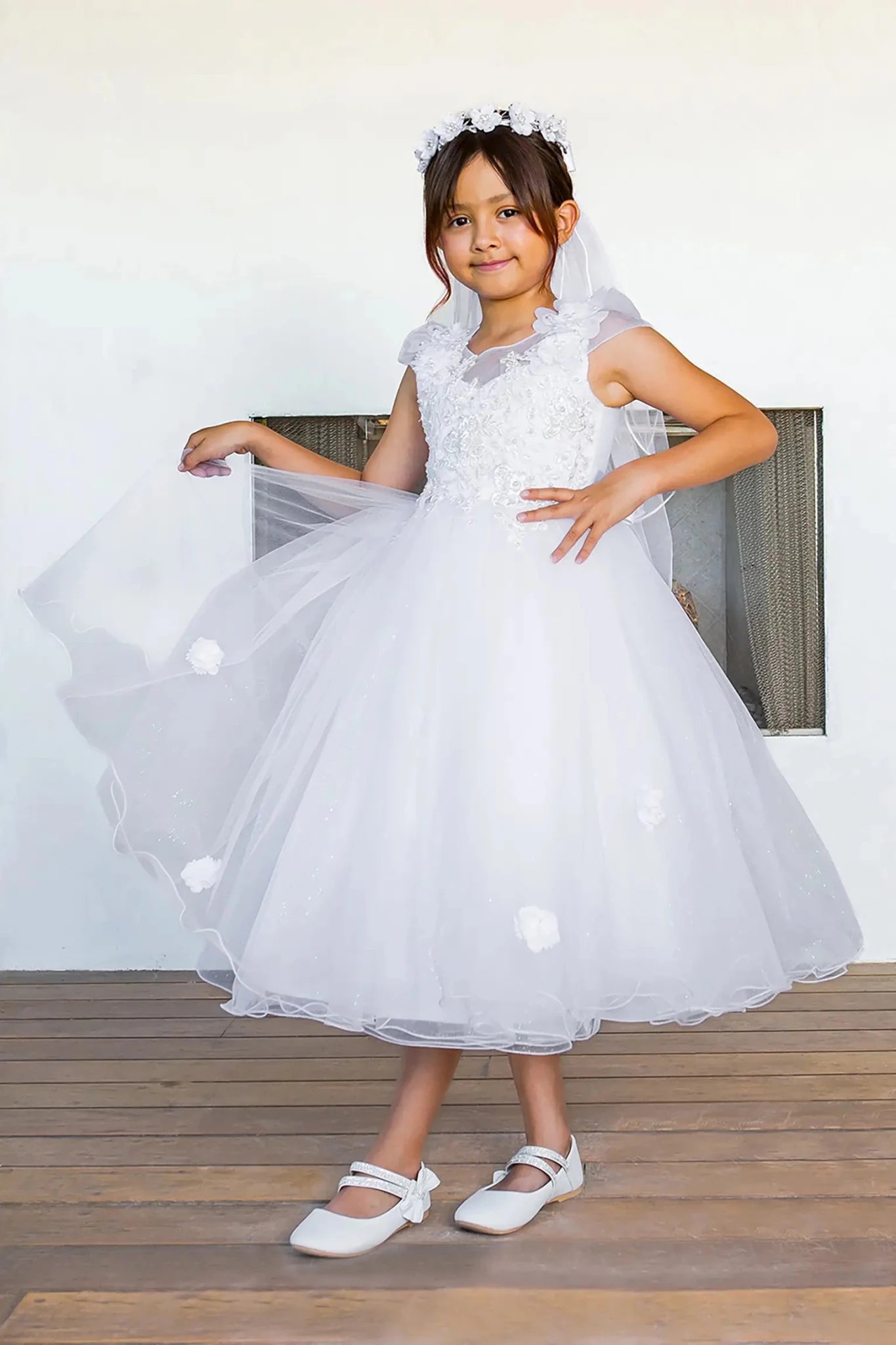 Young girl in a white lace dress with a veil standing indoors.