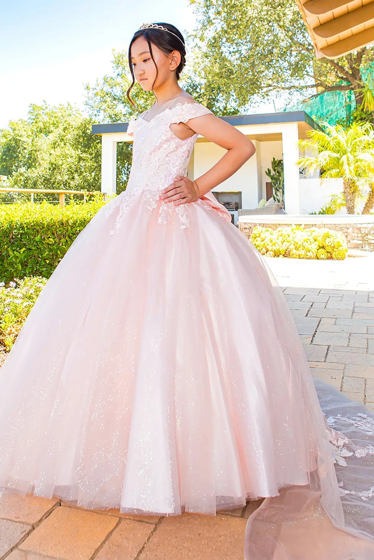 Young girl in a pink ball gown dress standing outdoors with greenery in the background