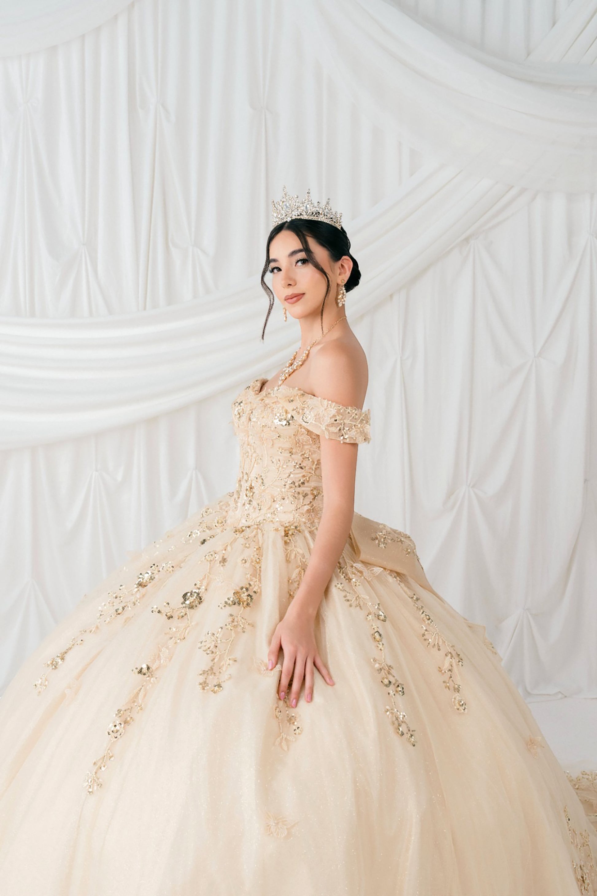 Woman in a champagne dress with floral details against a white draped curtain background
