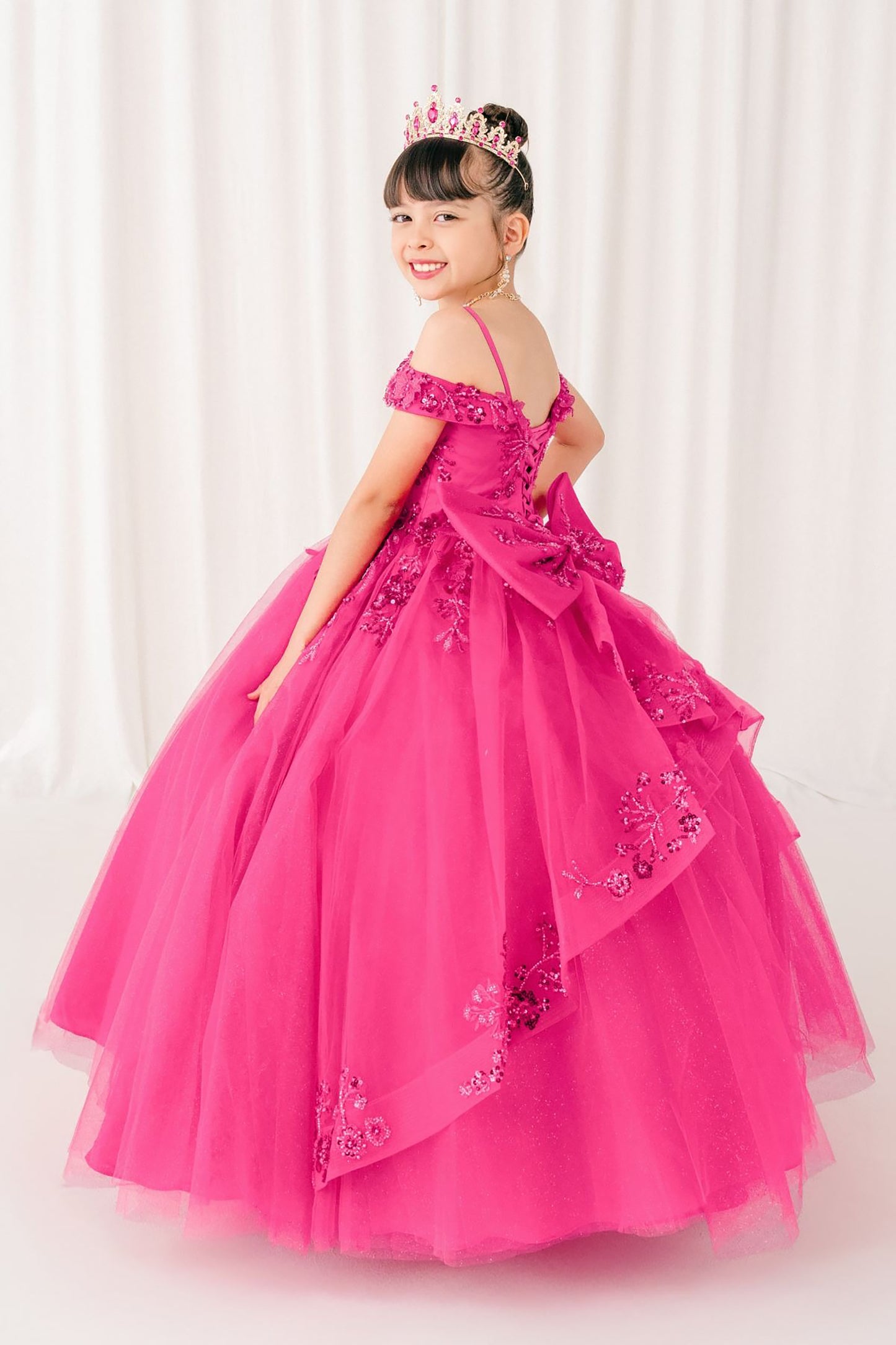 kid in a fuchsia mini quince dress with a tiara against a white curtain background