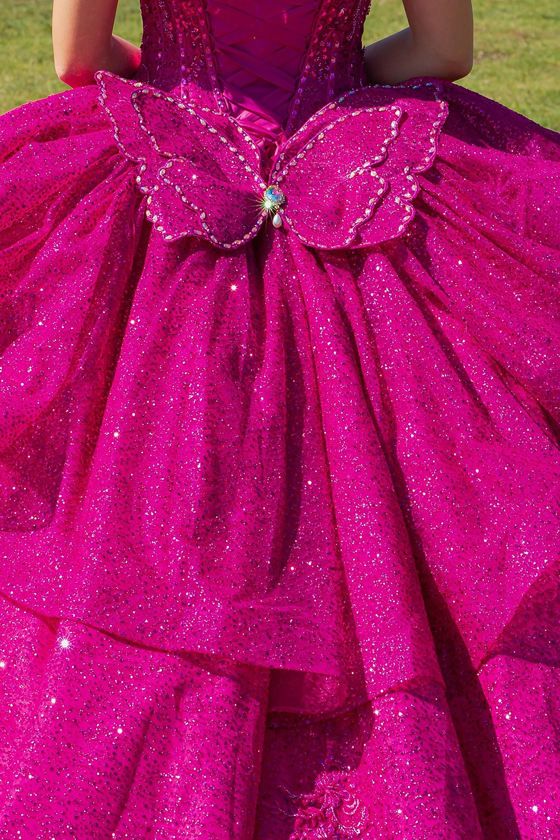 Close-up of a bright fuchsia glittery dress with a butterfly detail on a grassy background