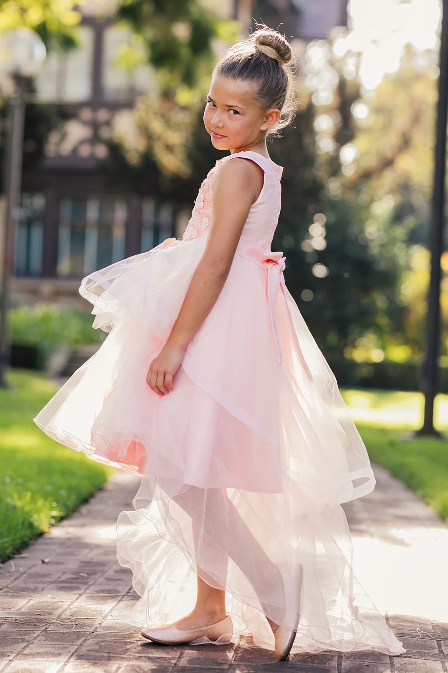 Young girl in a pink dress standing outdoors on a sunny day.