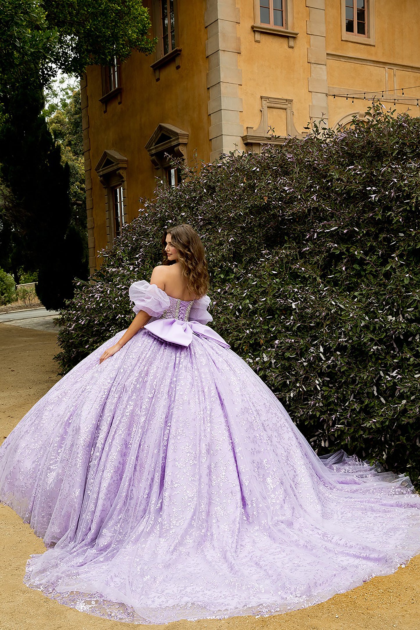 Woman in a lavender gown standing in front of a building with greenery