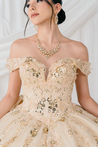 Woman wearing a champagne off-shoulder gown with sequin details and gold jewelry against a white background
