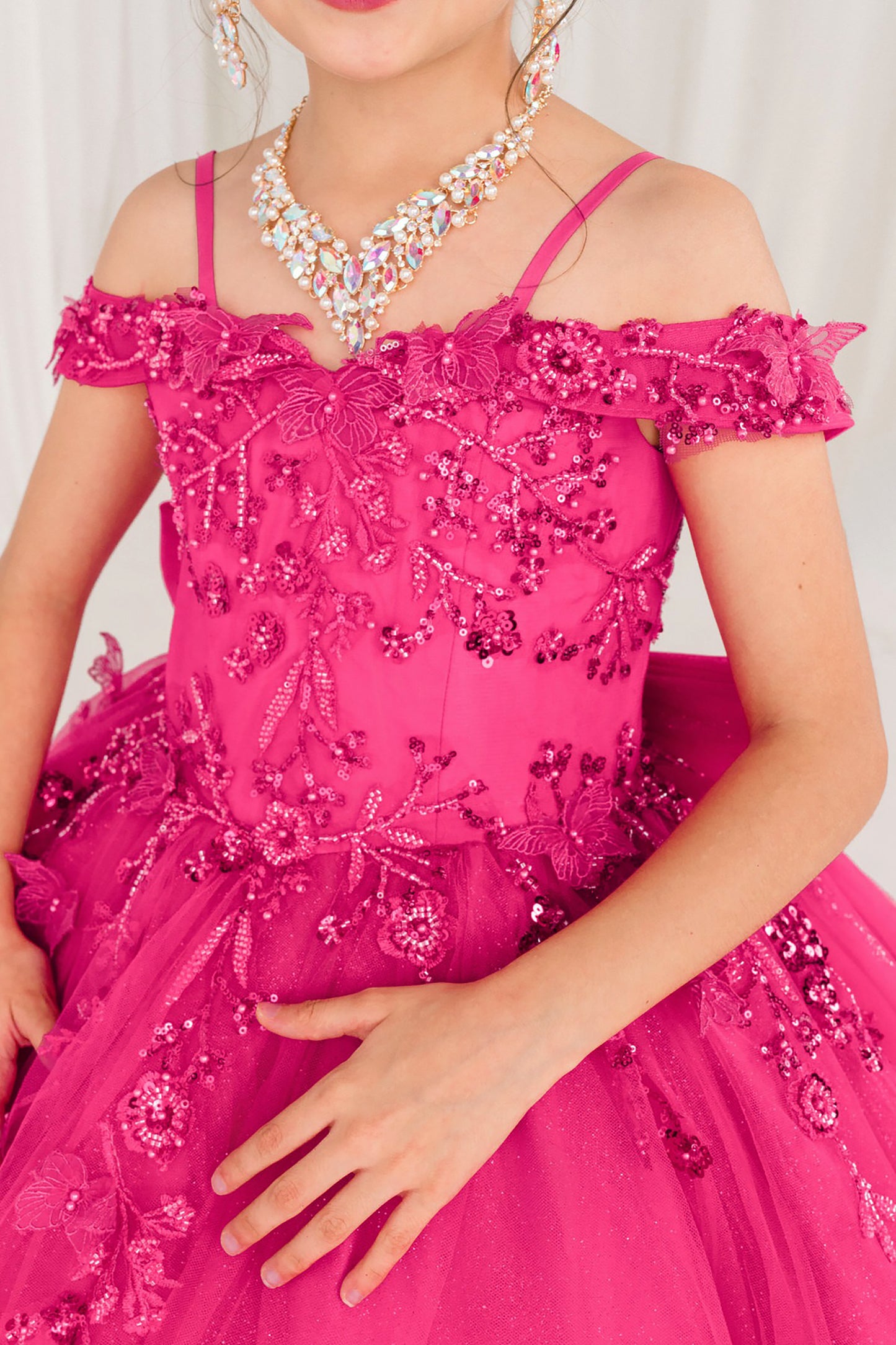Close-up of a kid wearing a fuchsia, beaded dress with a white background