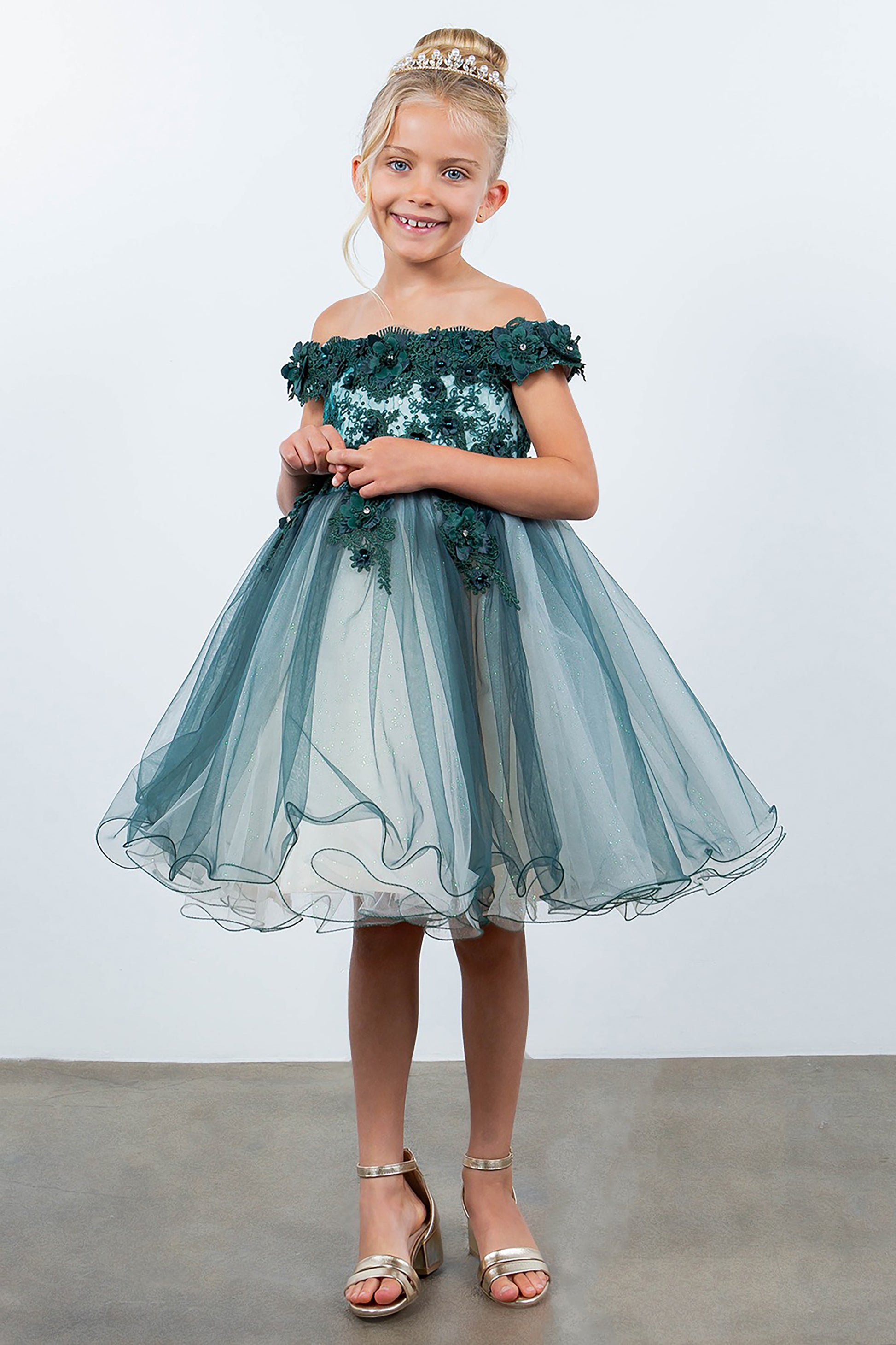 Young girl wearing a green off-shoulder dress with floral details against a white background