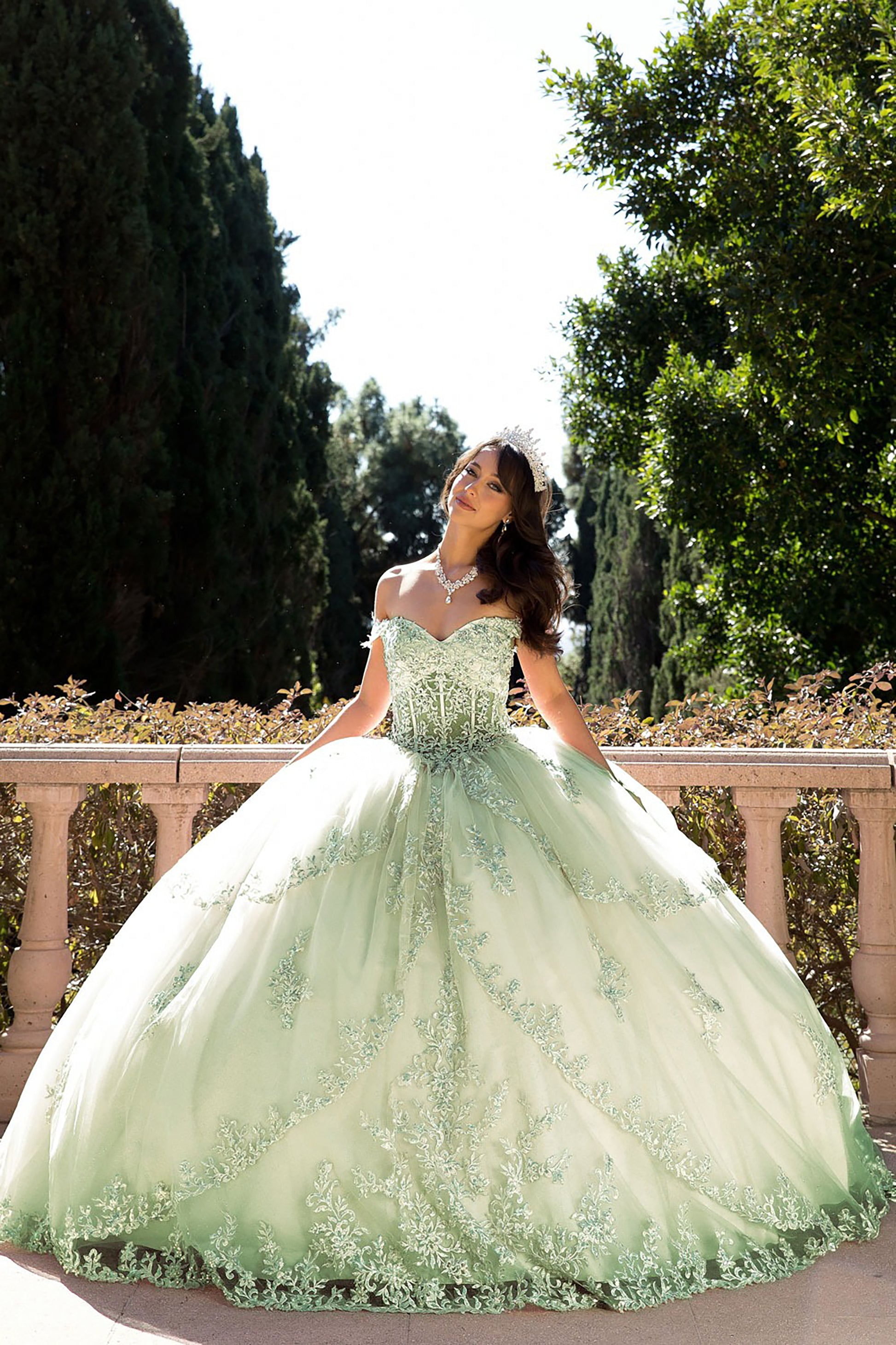 girl in a green sage formal quinceanera dress standing outdoors with trees in the background