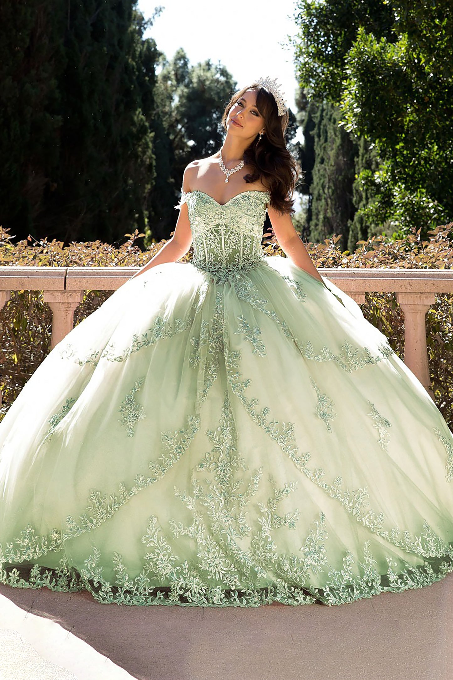 girl in a green sage quinceanera dress standing outdoors with trees in the background
