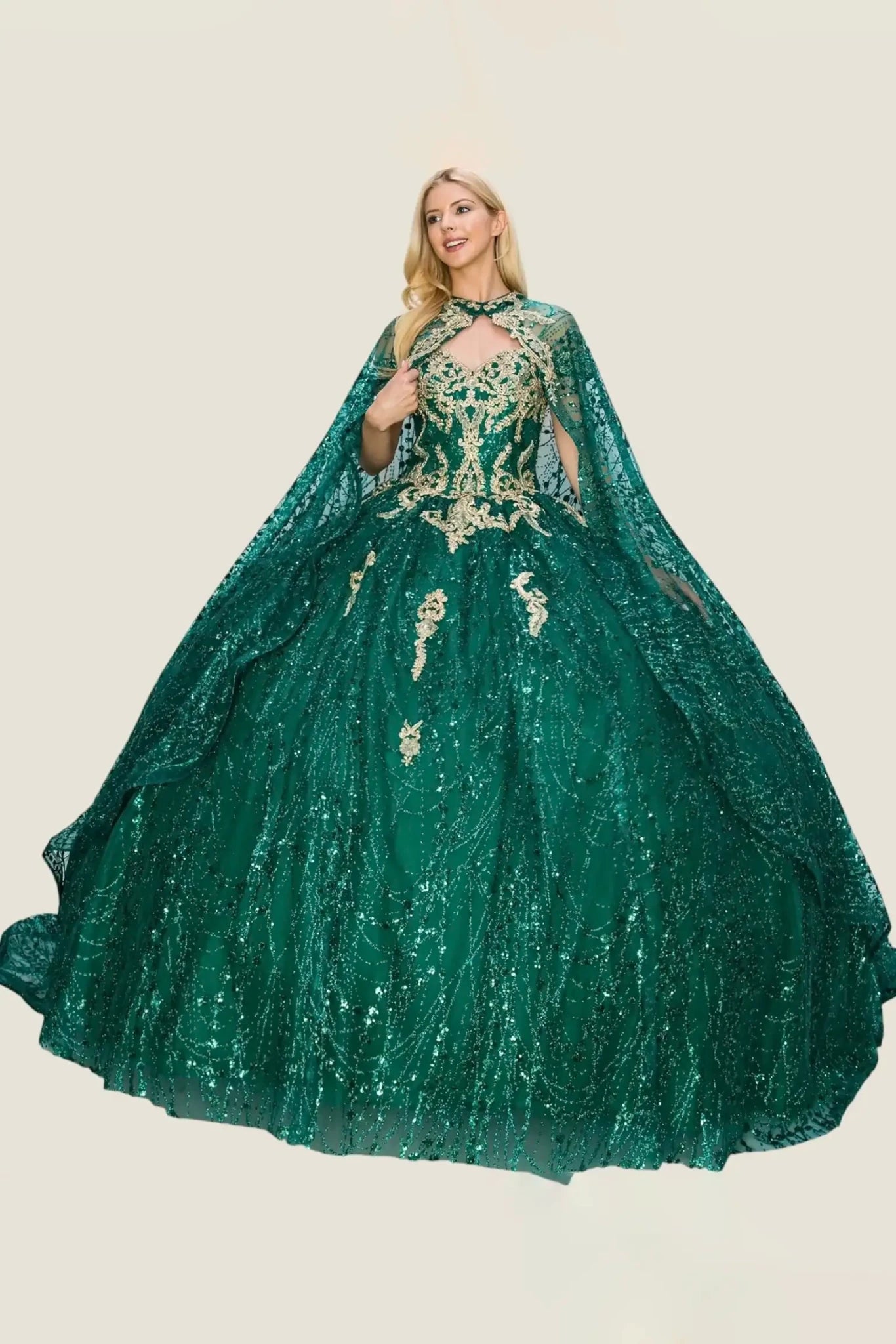 Woman standing front-facing in emerald green ball gown with gold embellishments, voluminous skirt, and draped cape