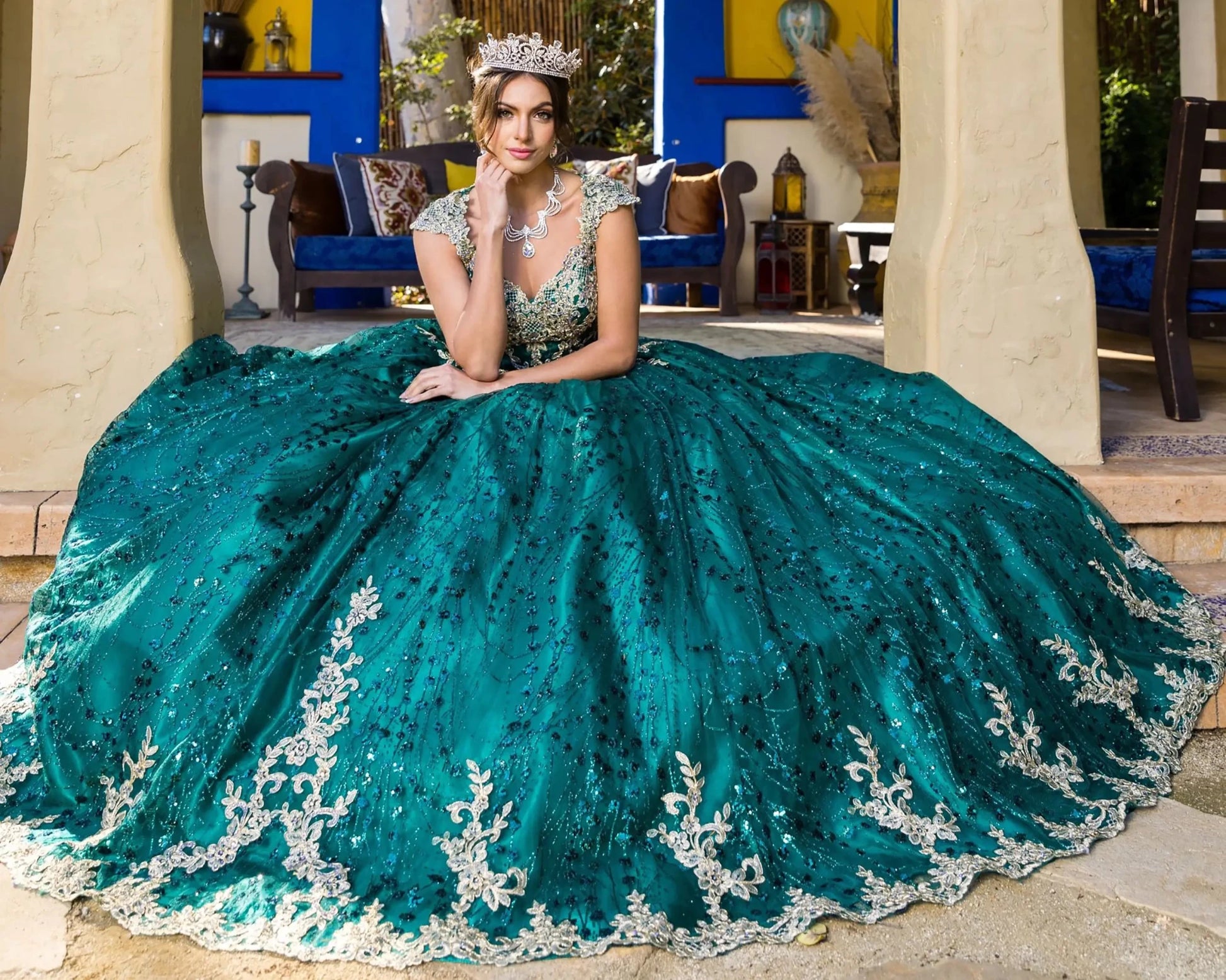 Woman in a green and silver gown with intricate detailing, standing in an elegant indoor setting.