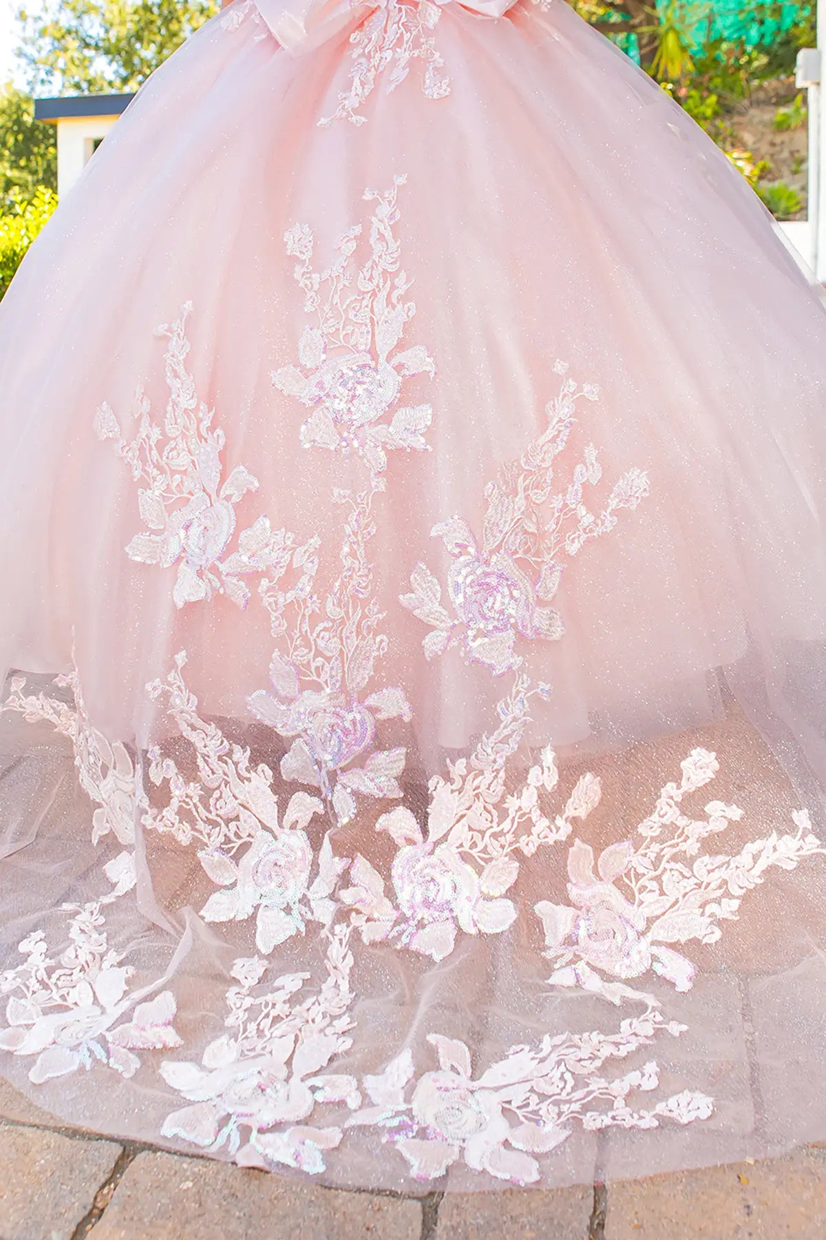 Pink tulle dress with floral lace details on a stone surface