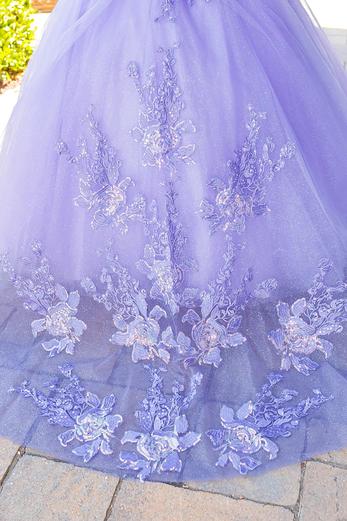 Close-up of a LIlac dress skirt with floral lace details on a stone surface.