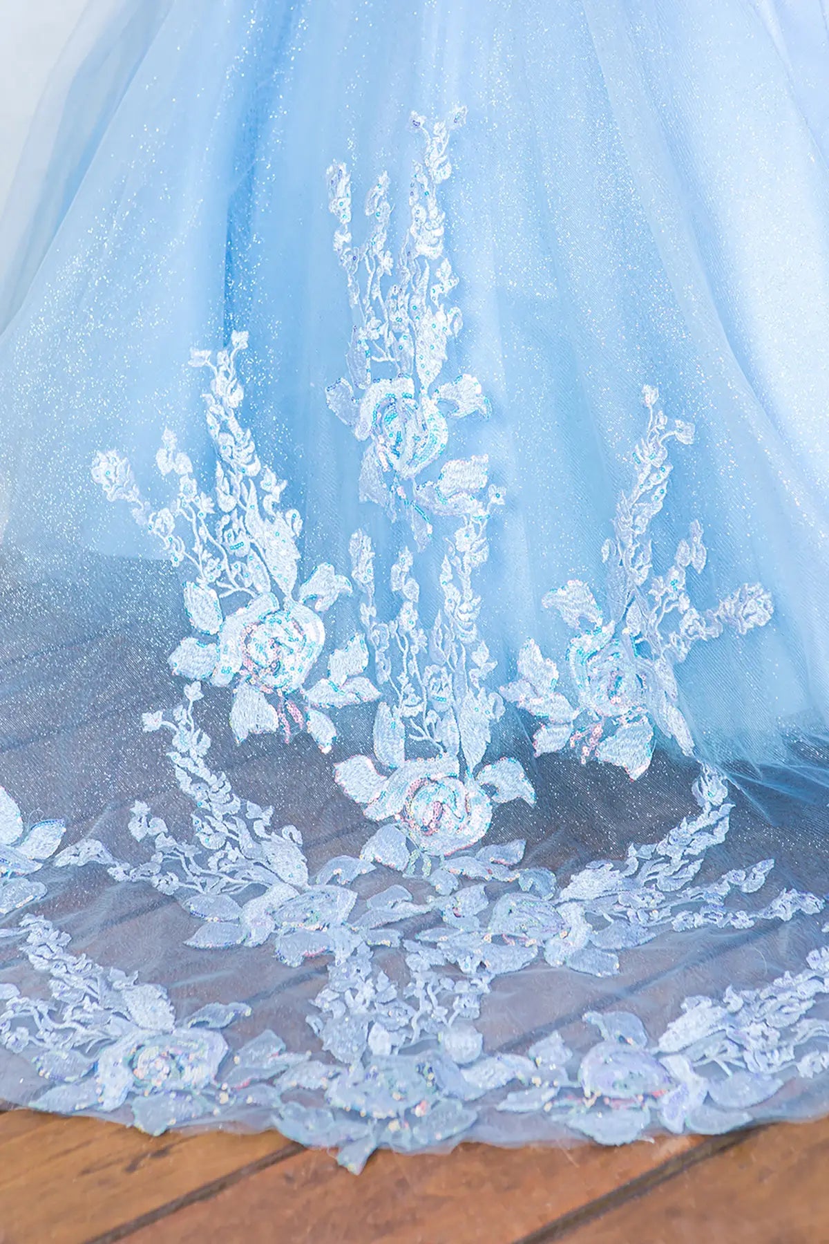 Close-up of a light blue lace fabric long train with floral patterns on a wooden surface.