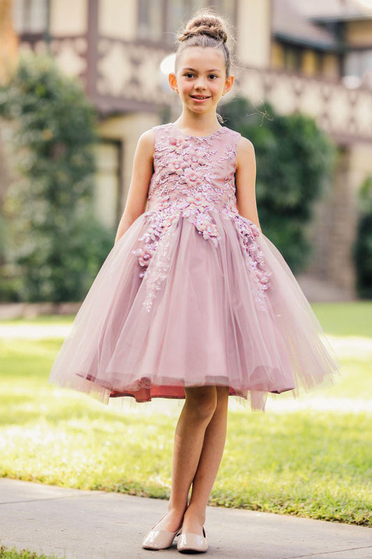 Young girl standing front-facing in mauve sleeveless flower girl dress with 3D floral appliqué bodice and wired layered tulle skirt