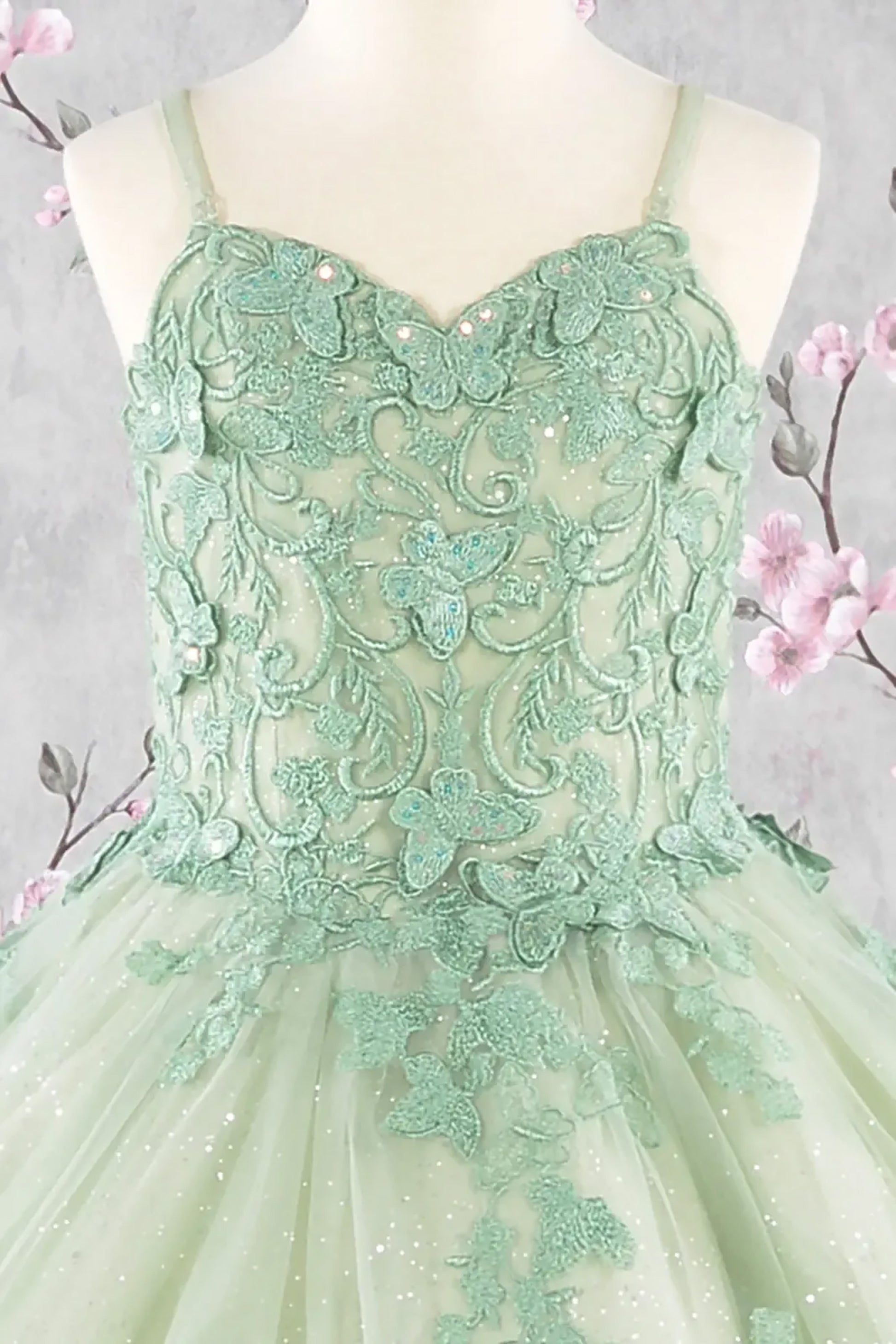 Green lace dress on a mannequin with a soft gray background and pink flowers.