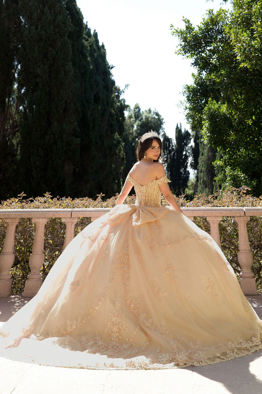Girl in a champagne quinceanera standing outdoors with greenery in the background