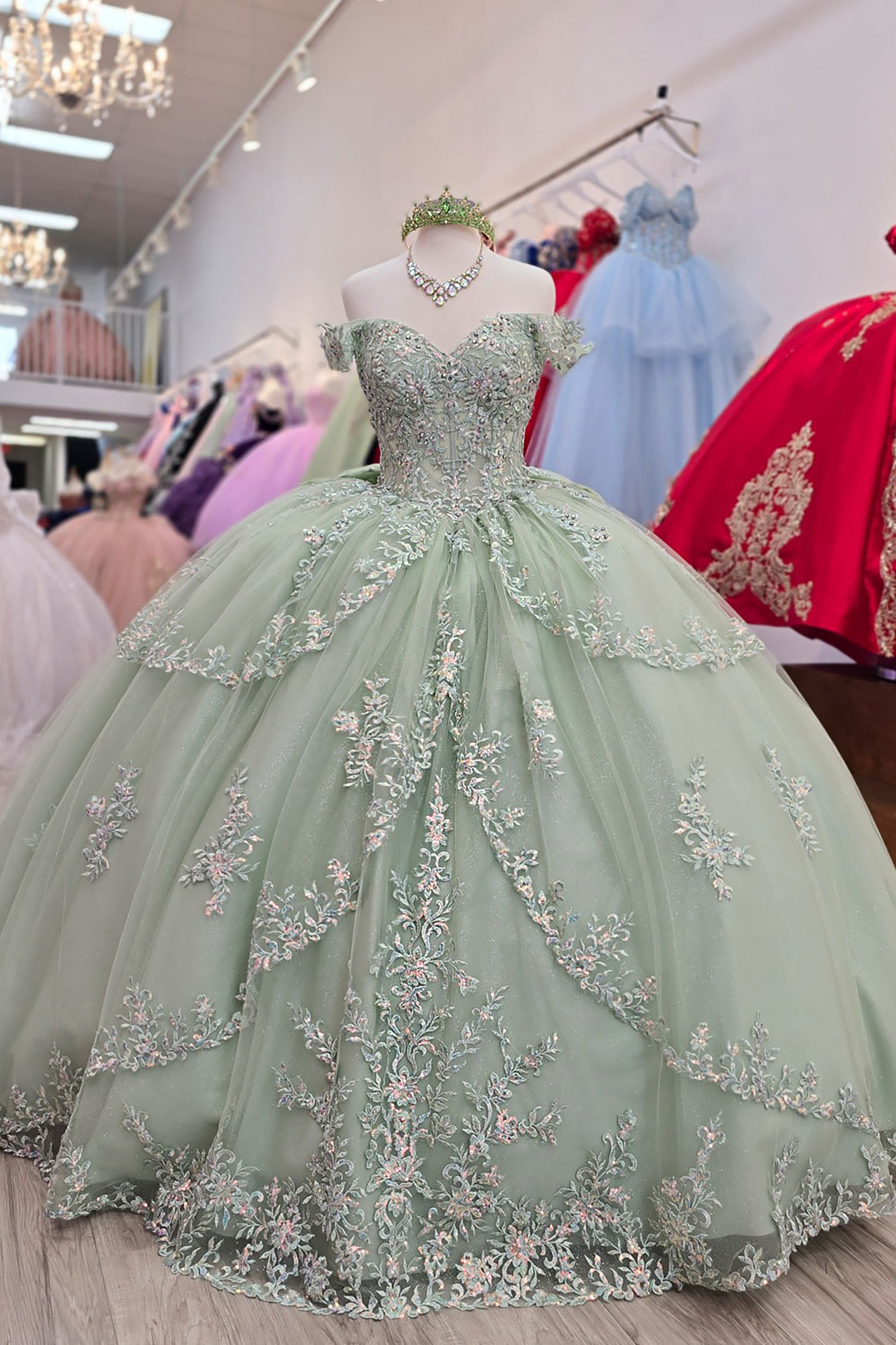 Sage green ball gown with floral embroidery on a mannequin in a store setting.