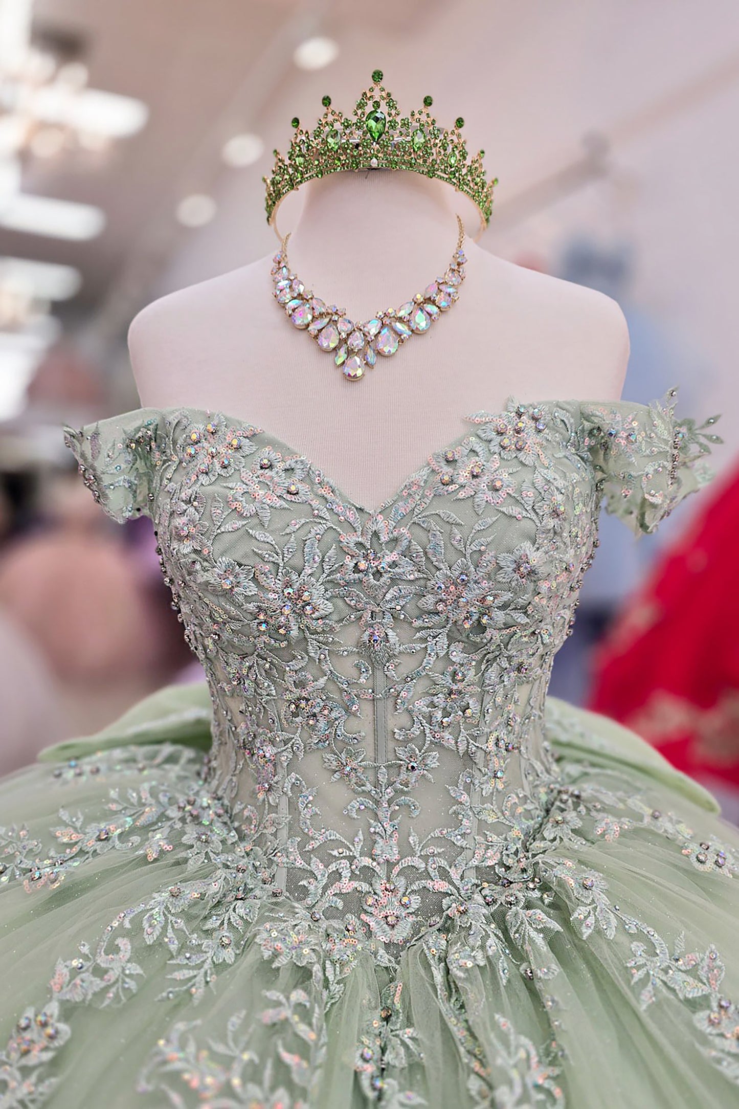 Green ball gown with intricate beadwork and a matching tiara on a mannequin.
