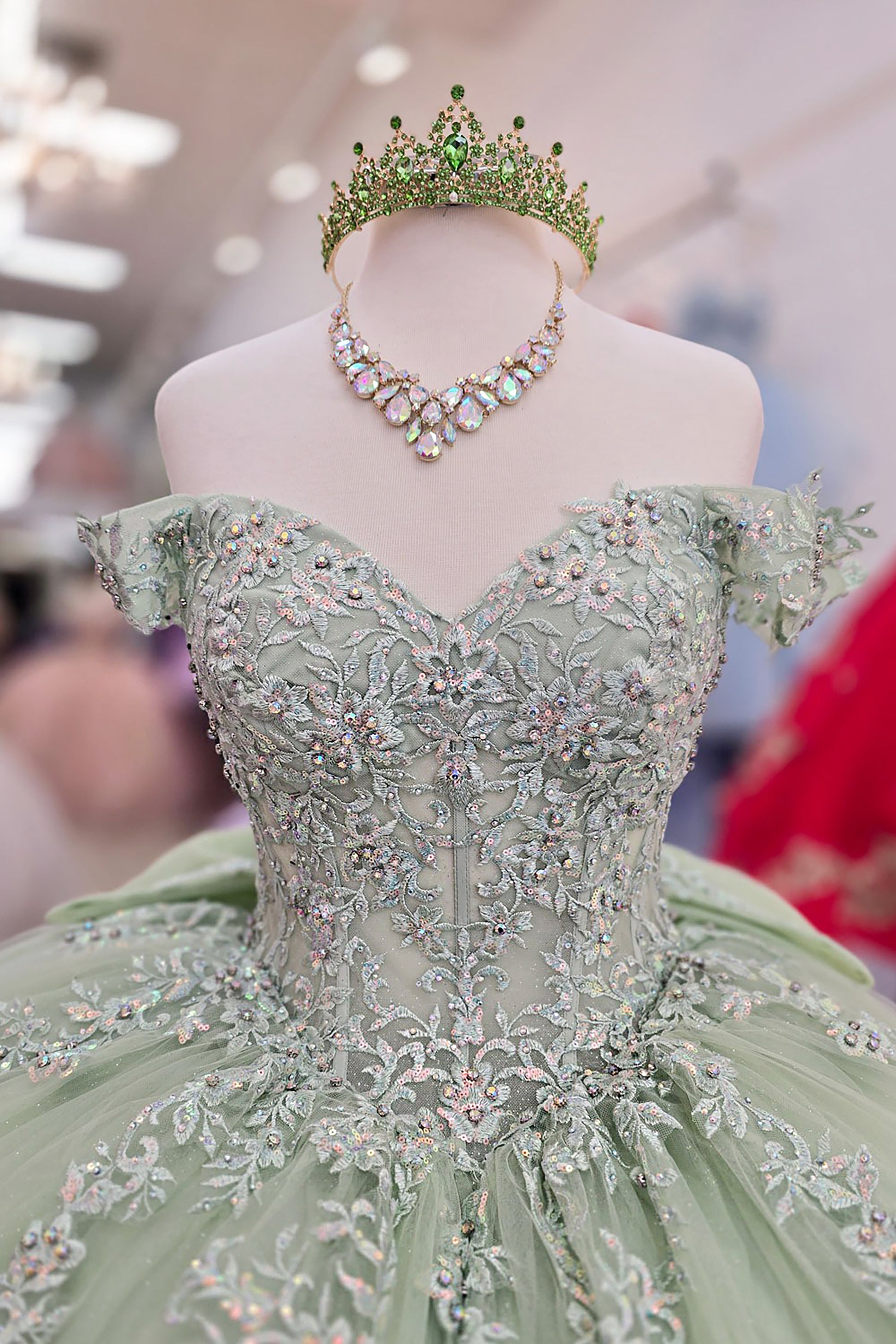 Green ball gown with intricate beadwork and a matching tiara on a mannequin.