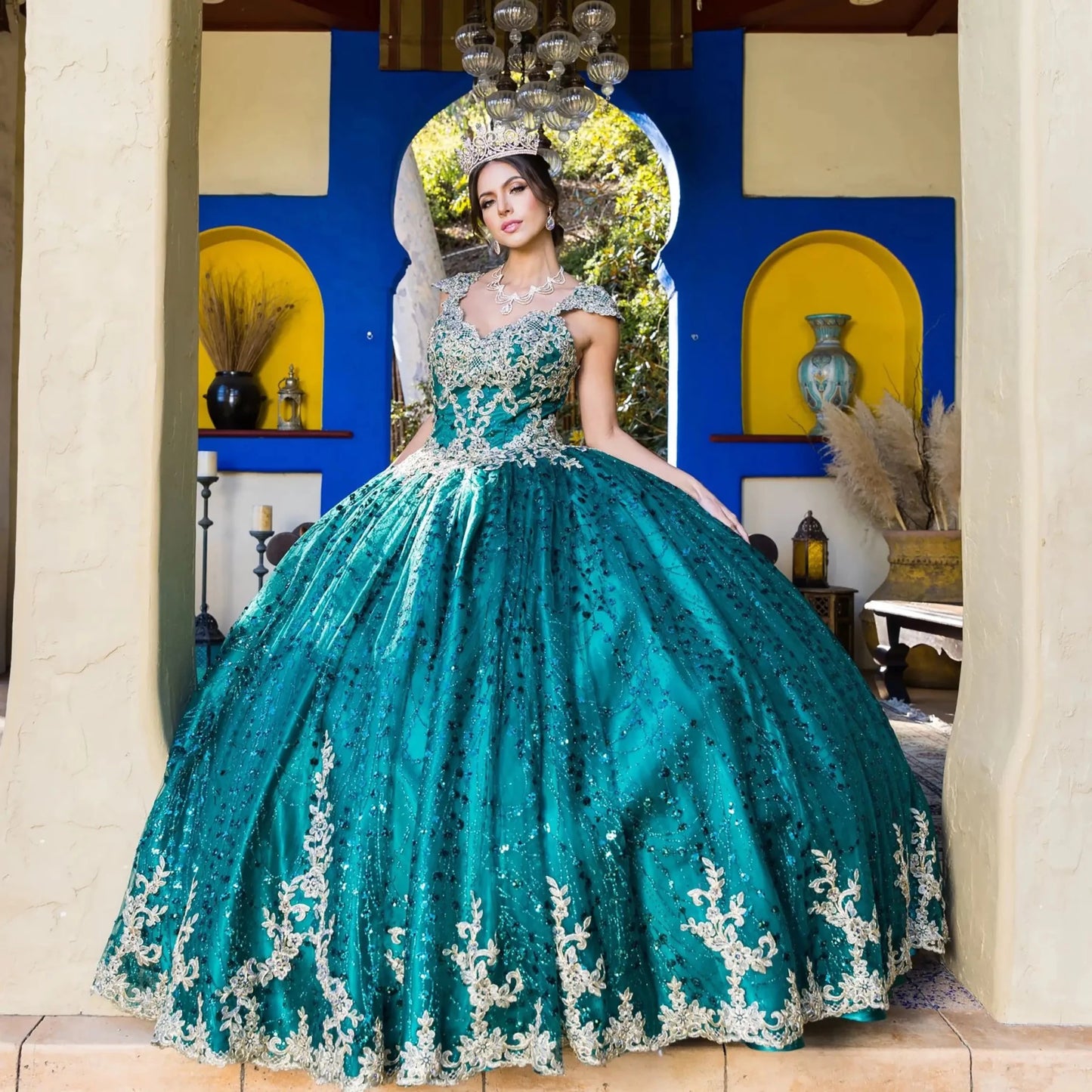 Woman in a teal and silver quinceañera dress standing in a decorated room.