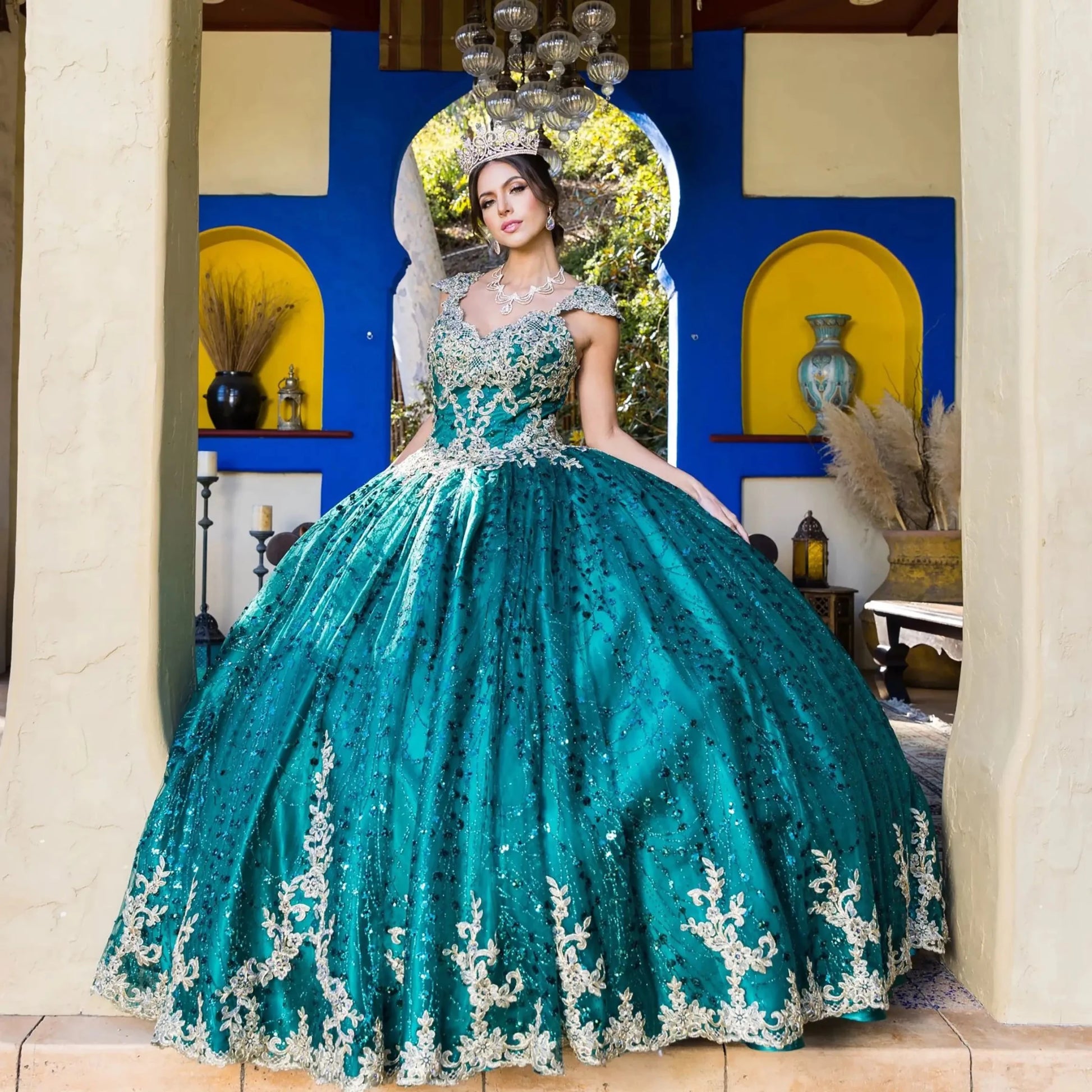 Woman in a teal and silver quinceañera dress standing in a decorated room.