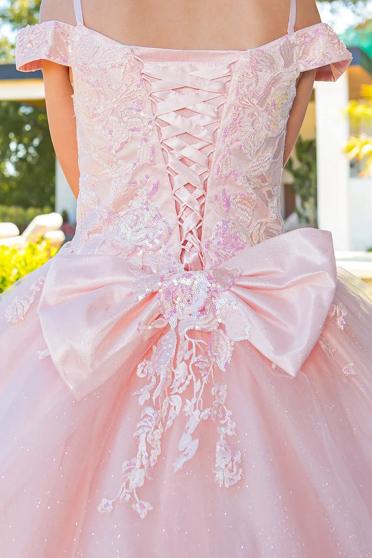 Pink off-shoulder dress with lace details and a large bow at the back, outdoor setting.