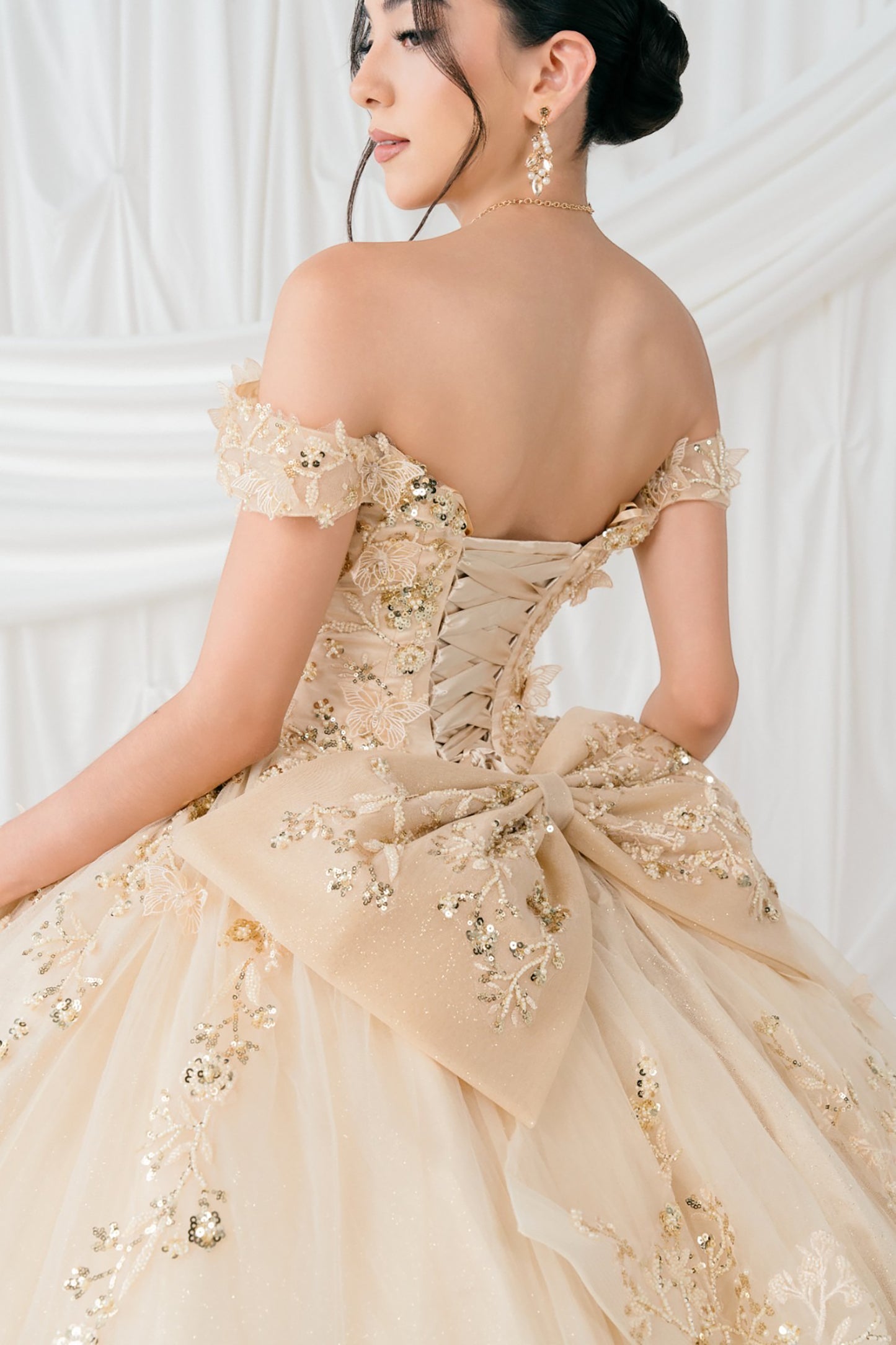 Woman wearing a champagne off-shoulder gown with floral details against a white background
