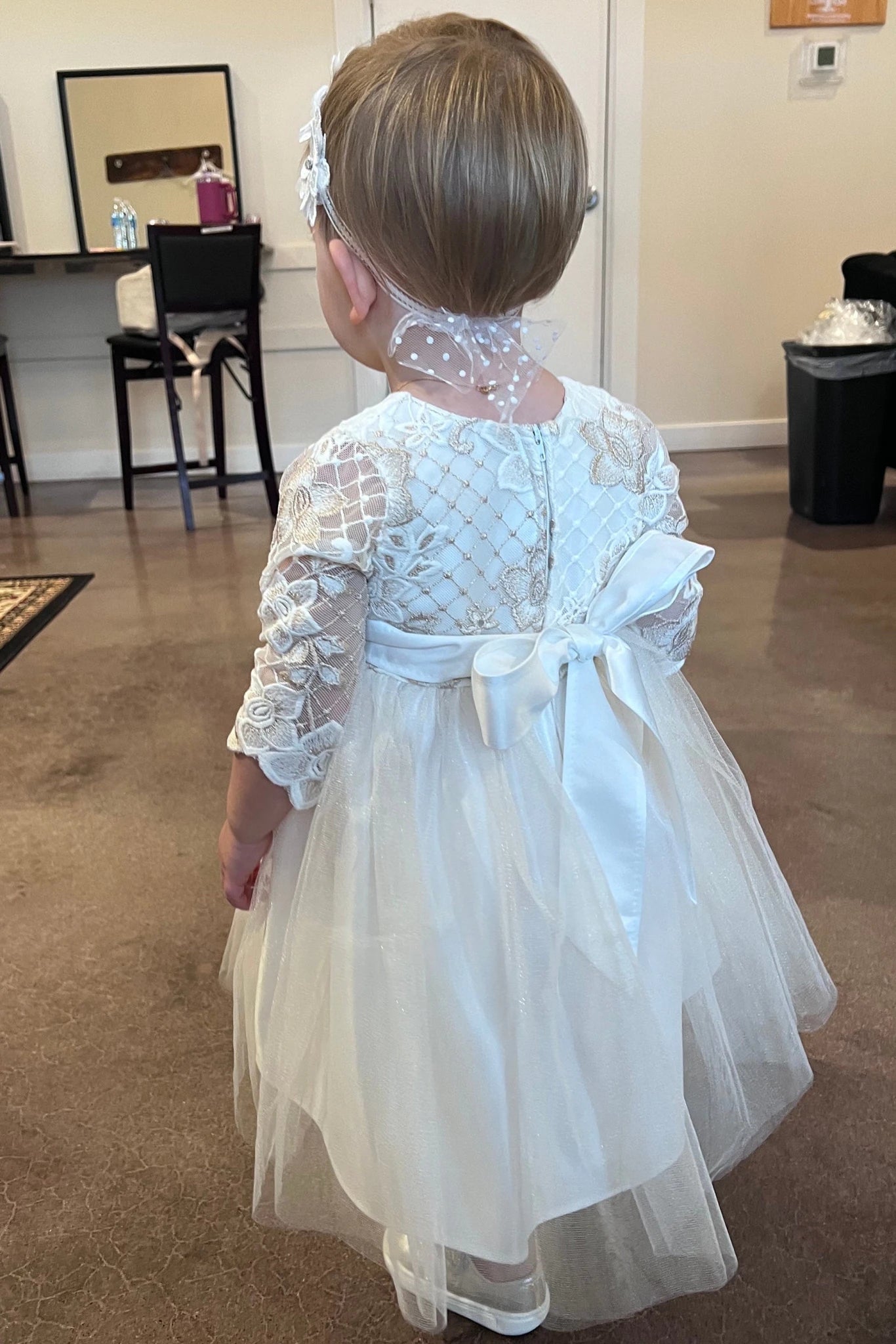 Child wearing a long sleeve white lace dress with a bow