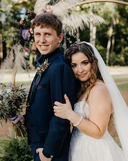 Couple on their wedding day with a decorated arch and greenery in the background and the bride is wearing a gold star shaped headband