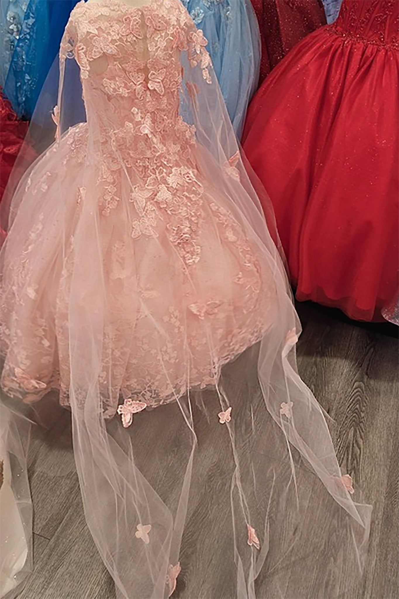 Pink floral mini quince dress with a long train in front of other dresses.