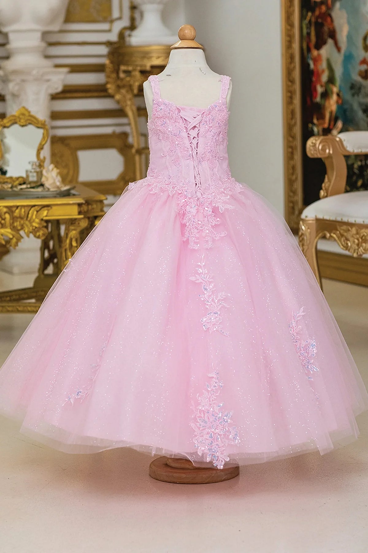 Behind the full skirt, the Pink mini quinceañera dress features corset lacing between floral appliqué panels.