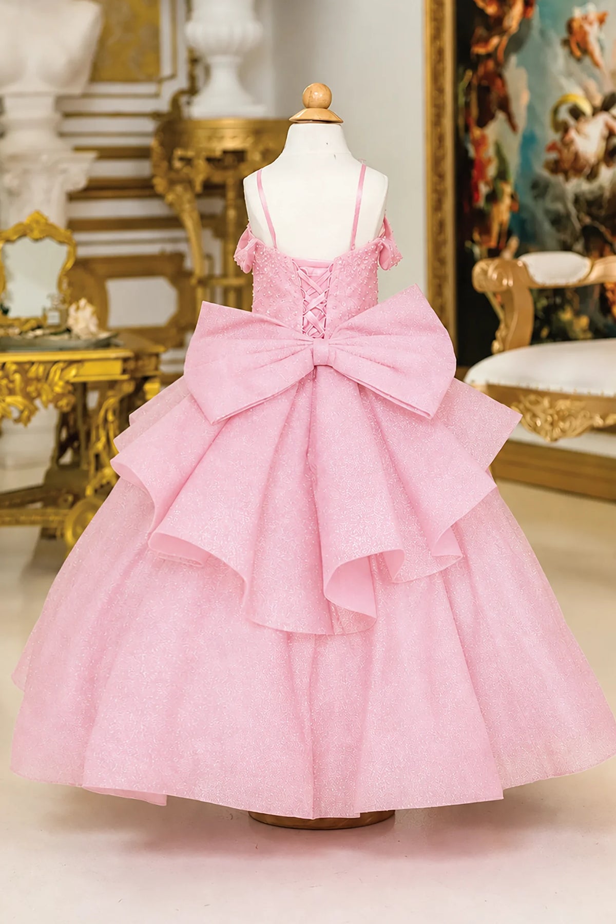 A light pink mini quince dress features a lace-up corset bodice, a very large matching bow at the back, and a tiered ruffled tulle skirt.