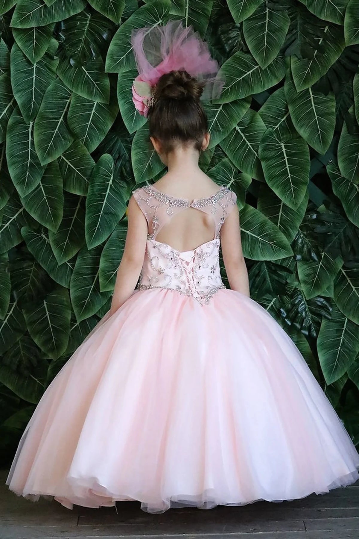 The reverse view reveals, the Blush Pink mini quince dress displays its lace-up finish and full tulle ball gown skirt with appliqué accents.