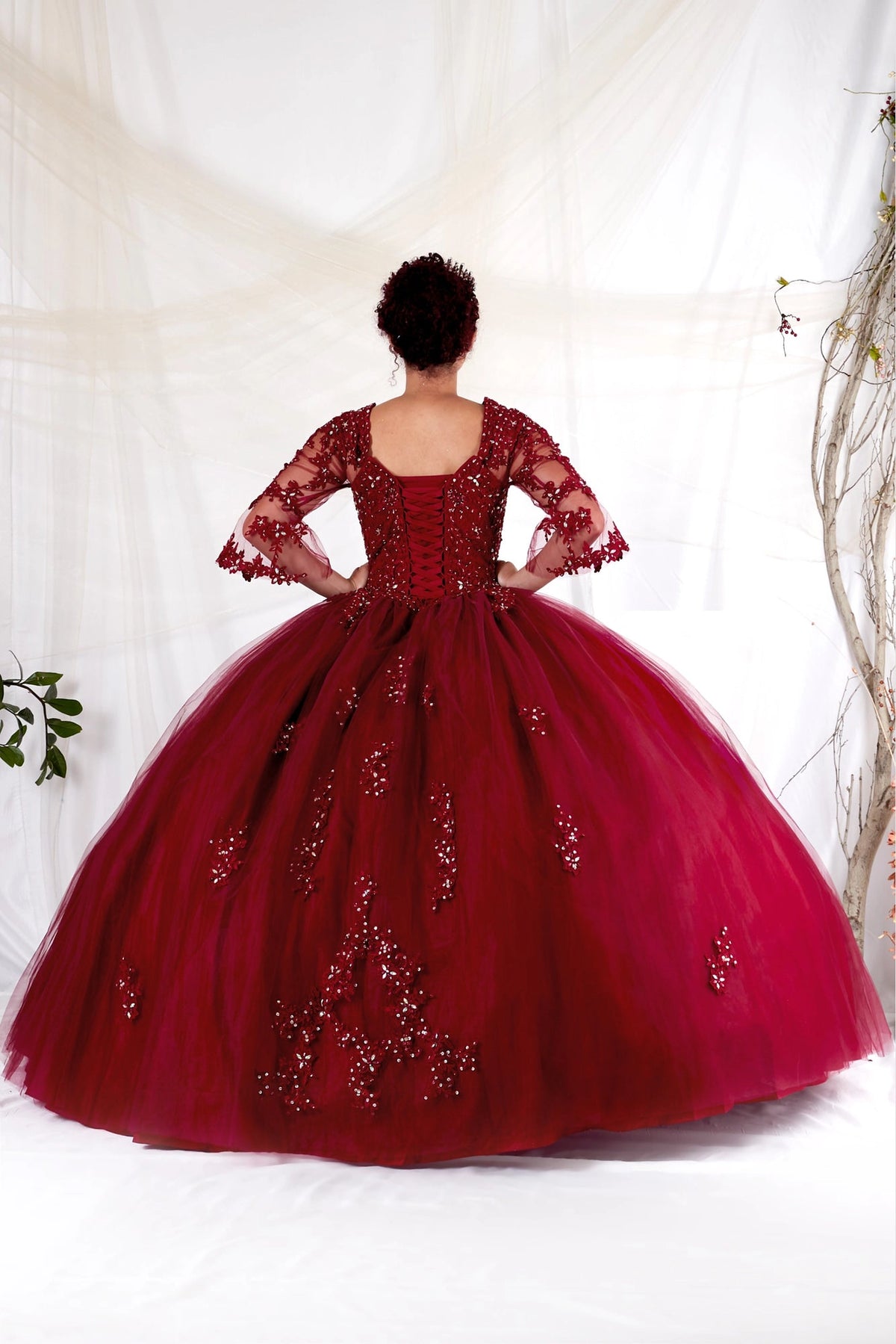 Corset lacing finishes the back of the Burgundy quinceañera ball gown beneath a low scoop neckline.