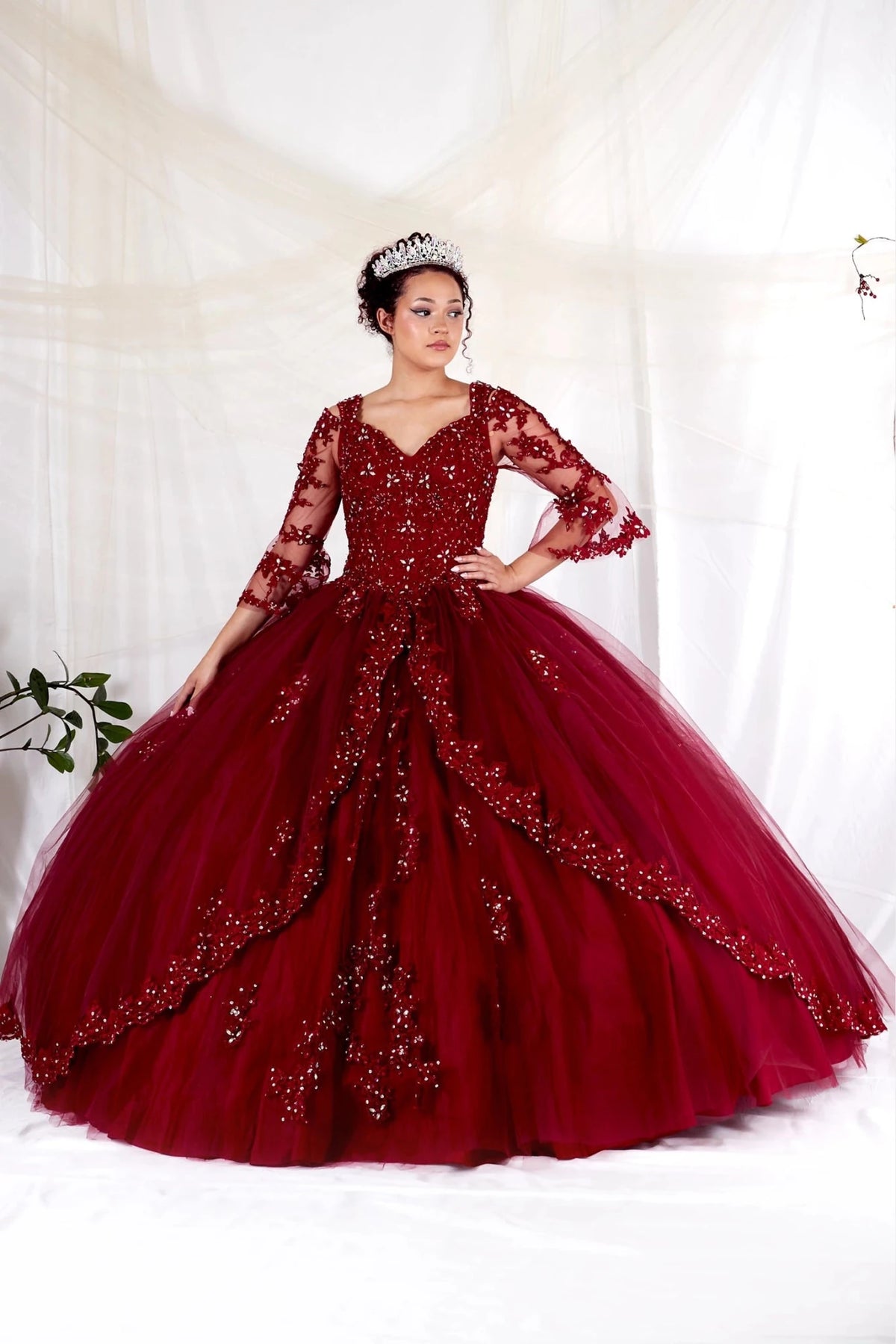 Ornate floral embroidery borders the sweeping skirt of this Burgundy quinceañera ball gown.