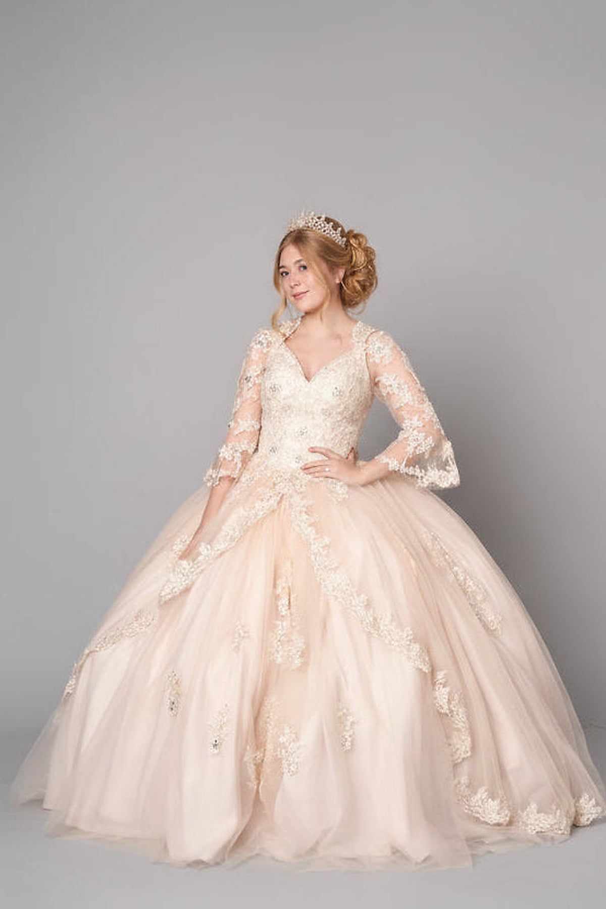 Champagne quinceañera ball gown shown from the side with long sheer sleeves and a full embroidered skirt.