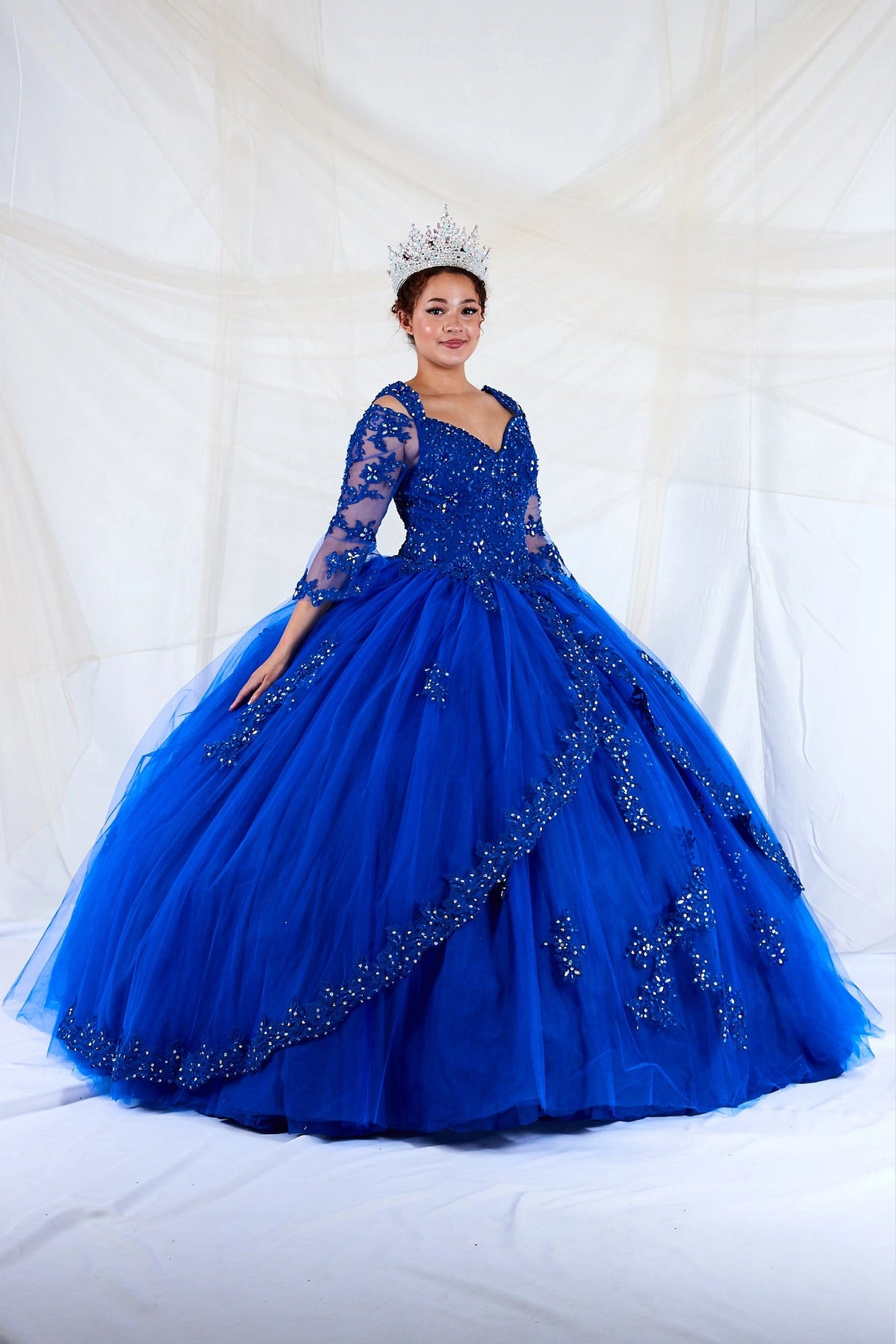 Layered floral embroidery sweeps over the full skirt of this Royal Blue quinceañera ball gown.