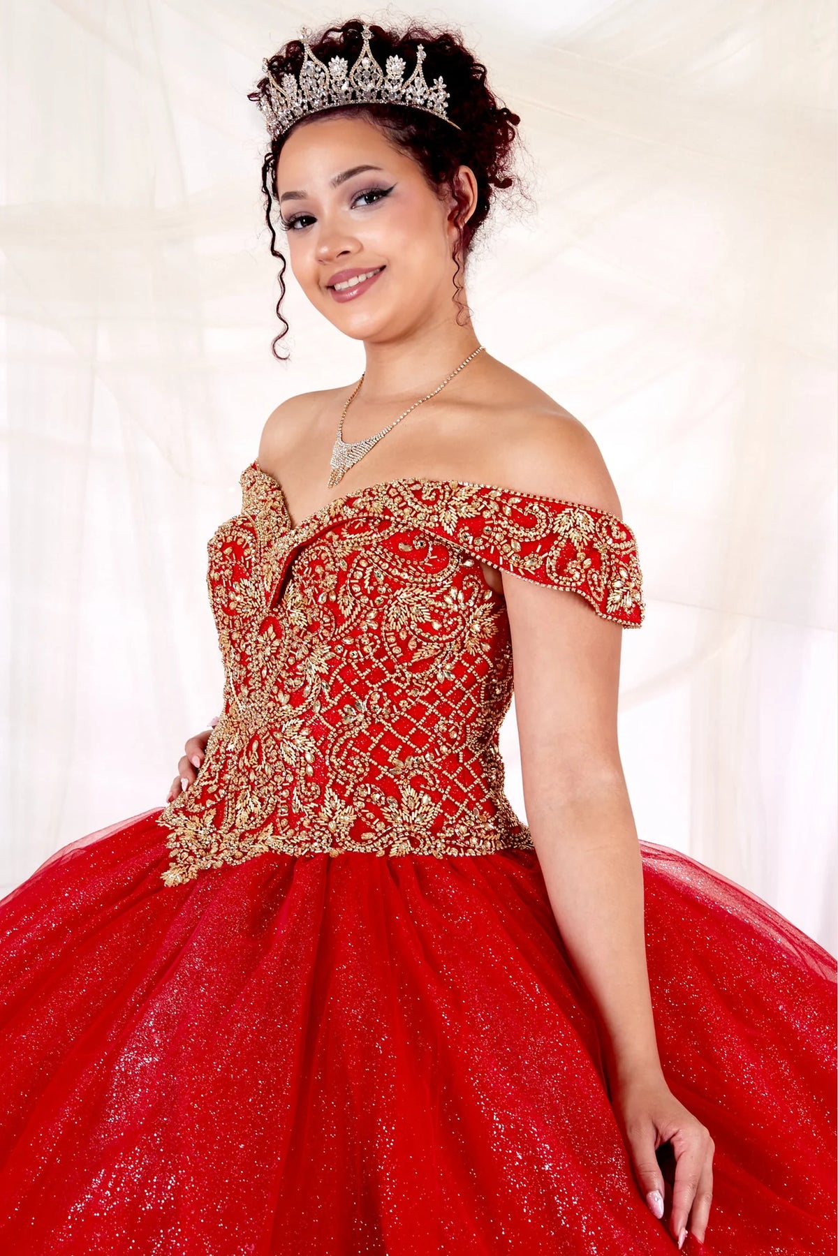 Off-shoulder floral embroidery and glitter tulle define the bodice detail of the Red/Gold quinceañera ball gown.