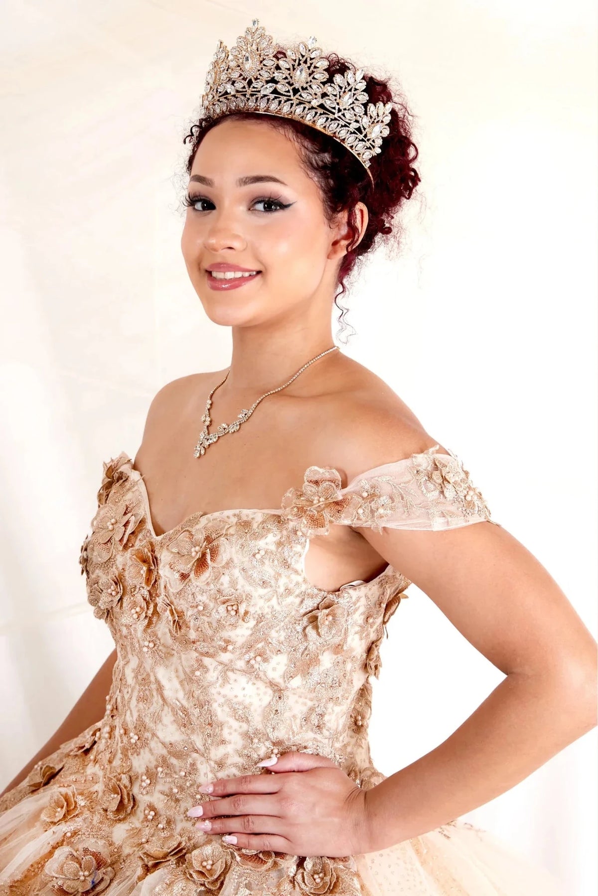 Dimensional floral appliqués and glitter accents defines the Champagne quinceañera dress in this detailed view.