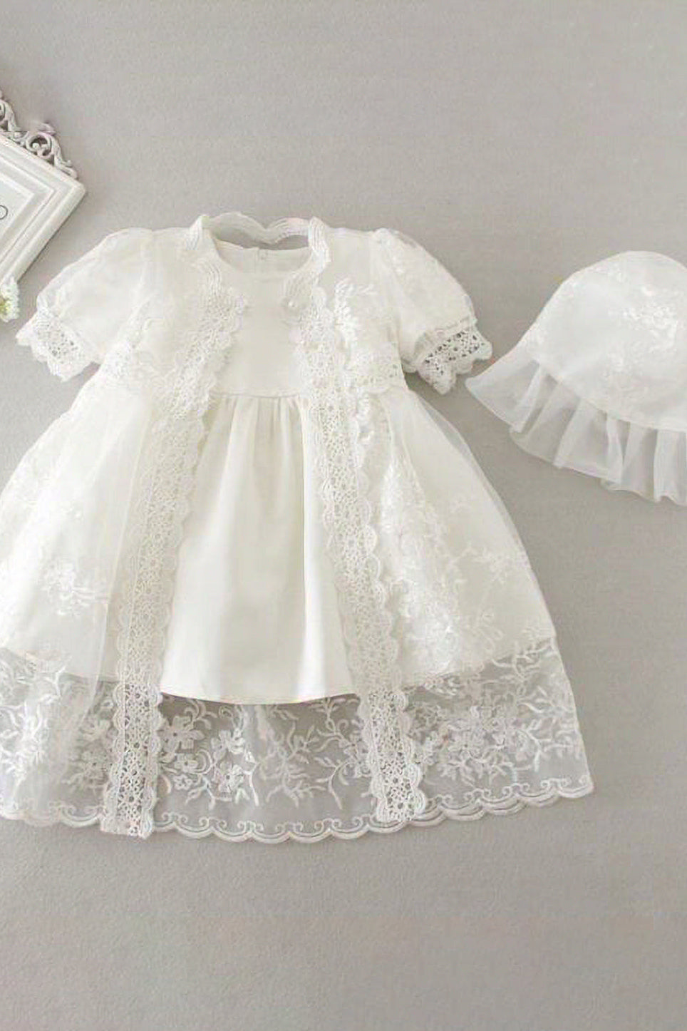 White lace baby dress with matching hat on a gray background