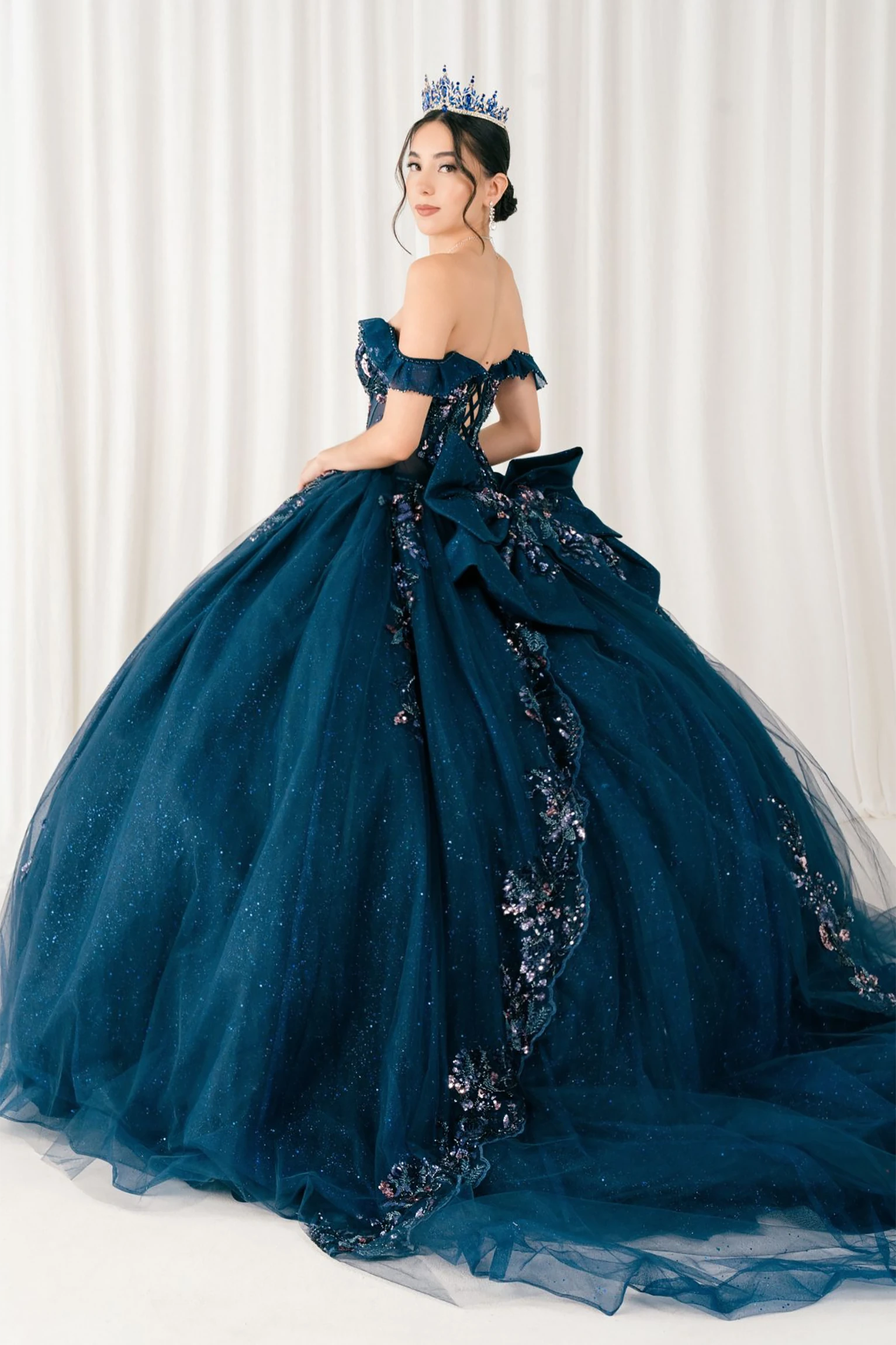 Woman wearing navy quinceañera royal dress side-facing with embroidered beaded corset bodice, shimmering textured skirt, detachable cape, cathedral train, and gloves