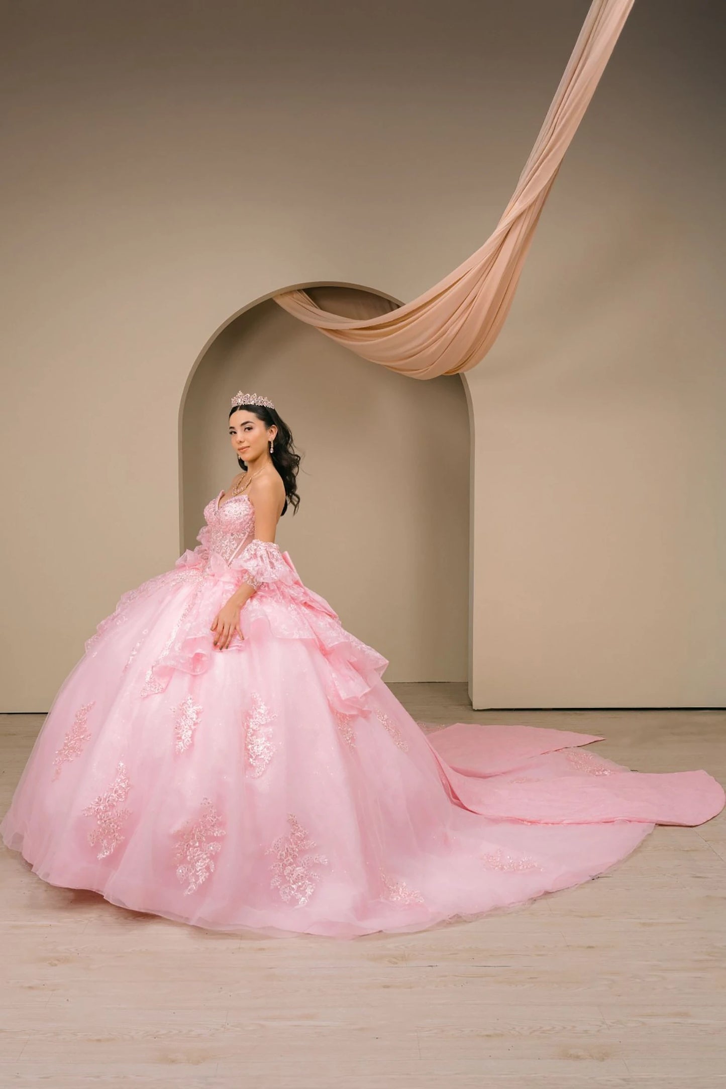 Woman wearing pink off-shoulder sweetheart quinceañera dress side-facing with beaded embroidered bodice, layered tulle organza skirt, and flowing silhouette